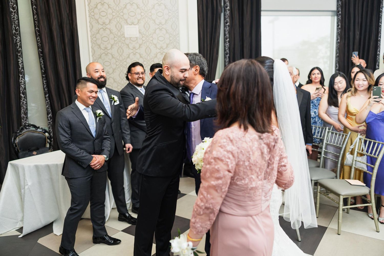 Wedding guests watch as couple exchanges vows in elegant ballroom with damask wallpaper.