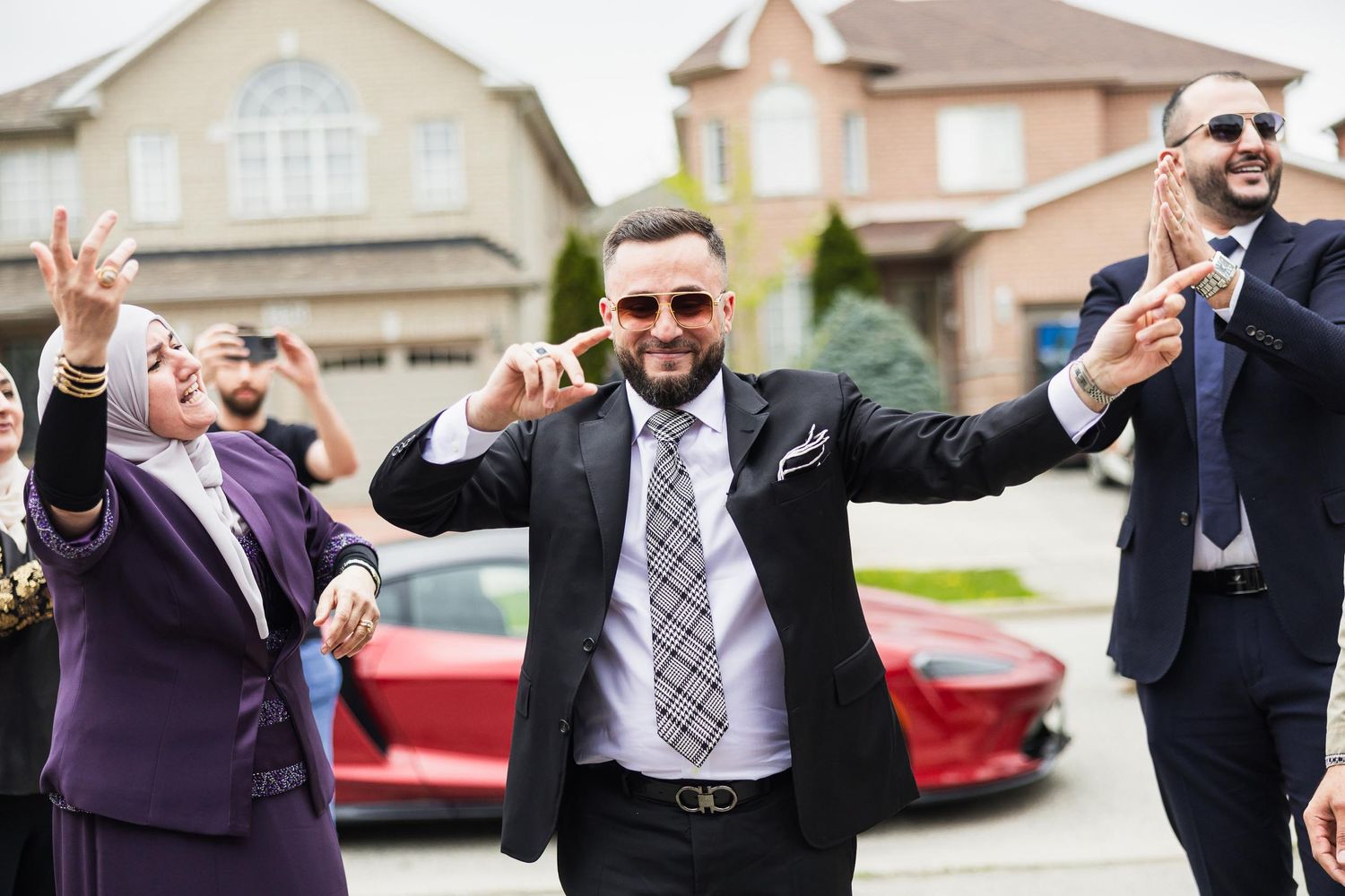 A celebratory moment with people in formal attire gesturing joyfully outside suburban homes.