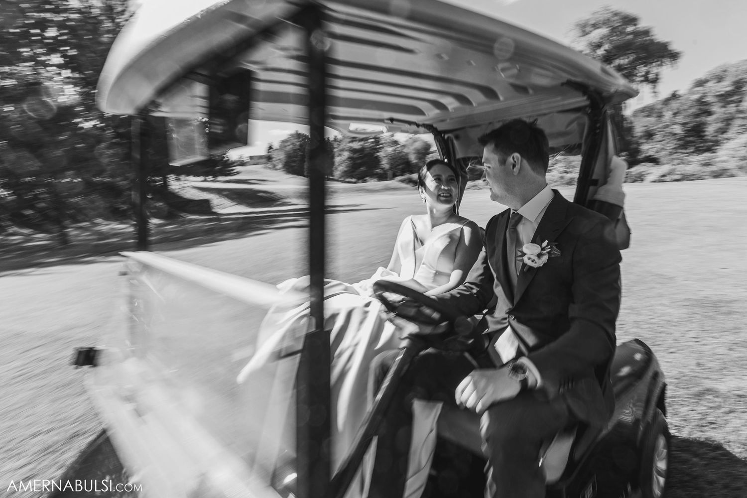 A black and white photo of newlyweds riding together in a golf cart.