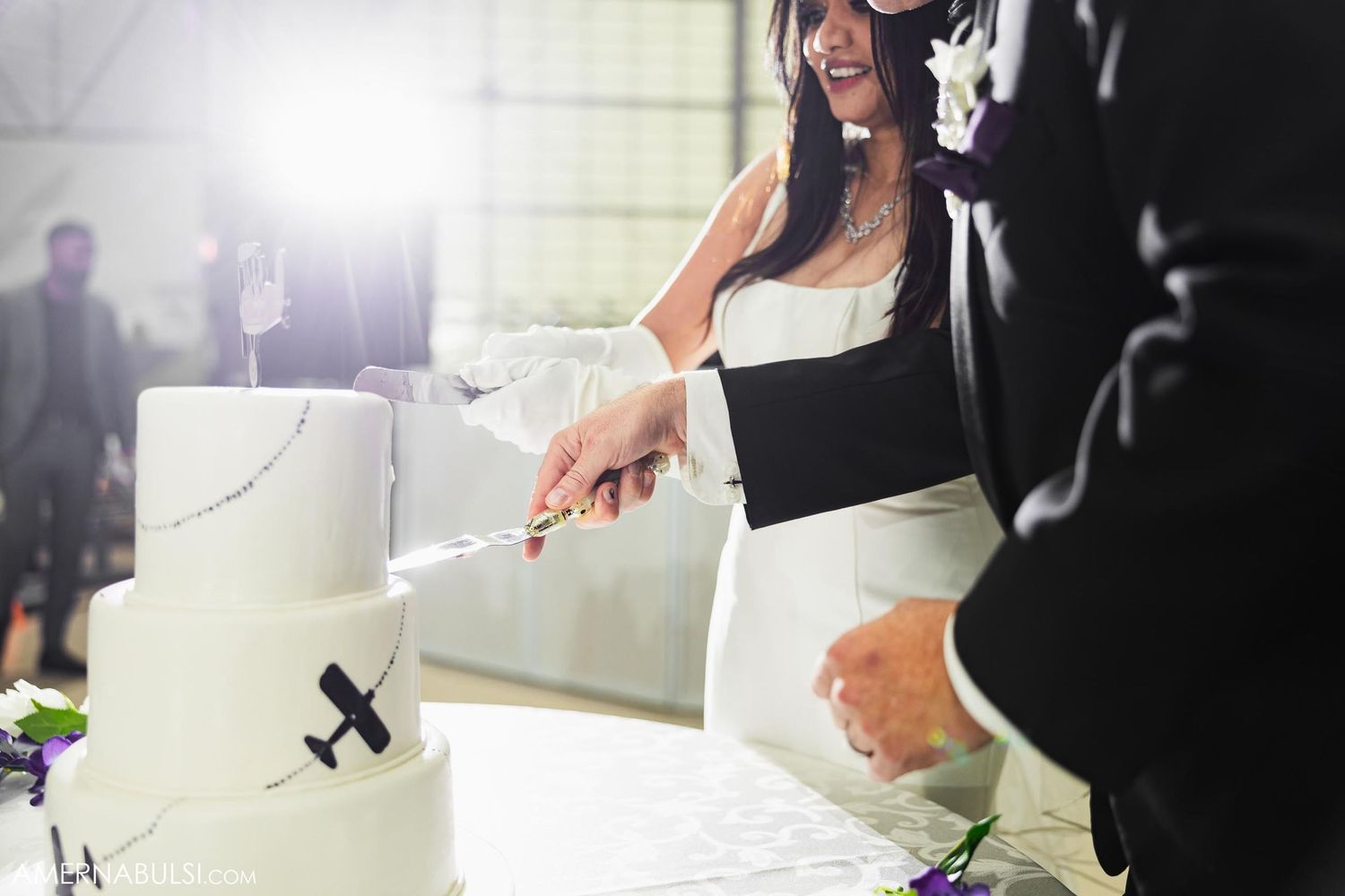 Bride cutting elegant white wedding cake at aviation-themed reception.