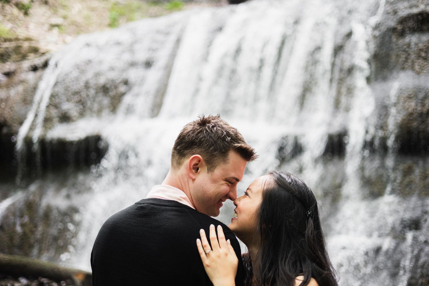 A couple shares an intimate moment in front of a cascading waterfall.