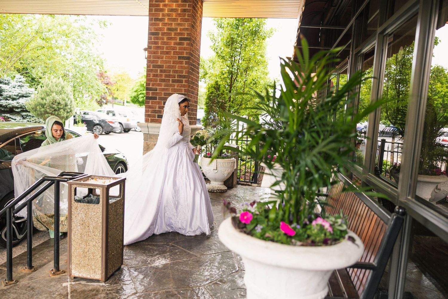 Bride in white dress stands near outdoor patio with floral planters.