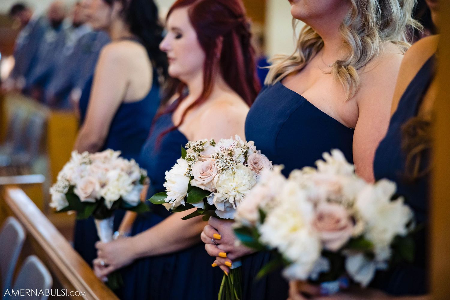 Bridesmaids in navy dresses holding pink and white floral bouquets during church ceremony.