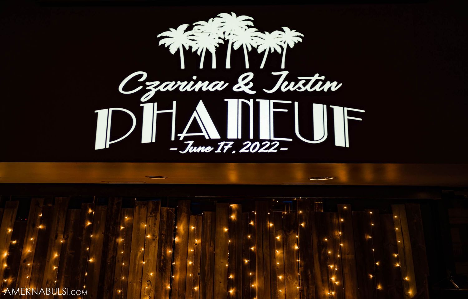 Illuminated wedding venue sign reading 'Dhaneuf' with palm tree design and string lights below.
