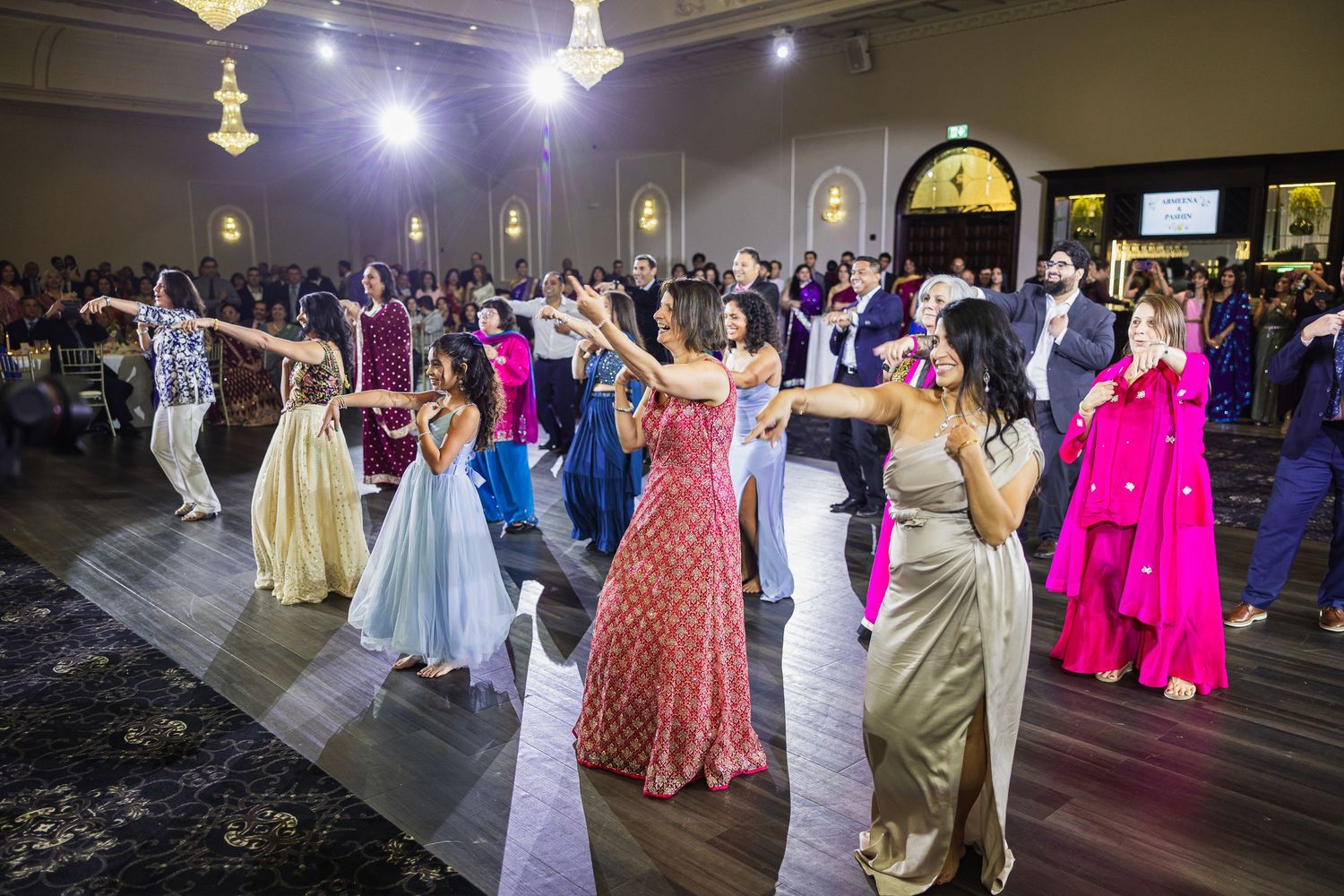 Wedding reception hall filled with guests in colorful formal attire dancing and celebrating.