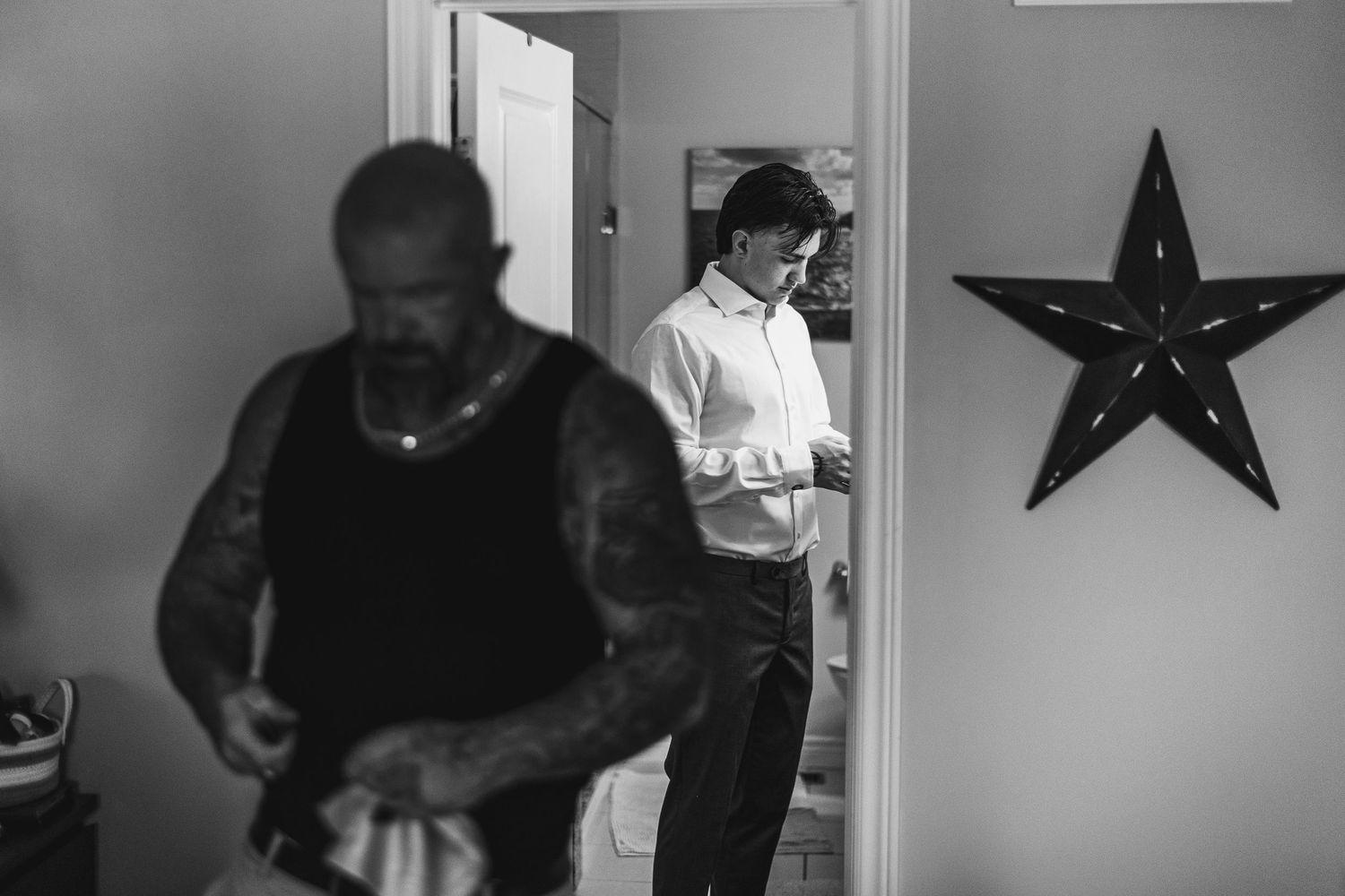 Two men getting dressed in black and white photo with decorative star on wall.