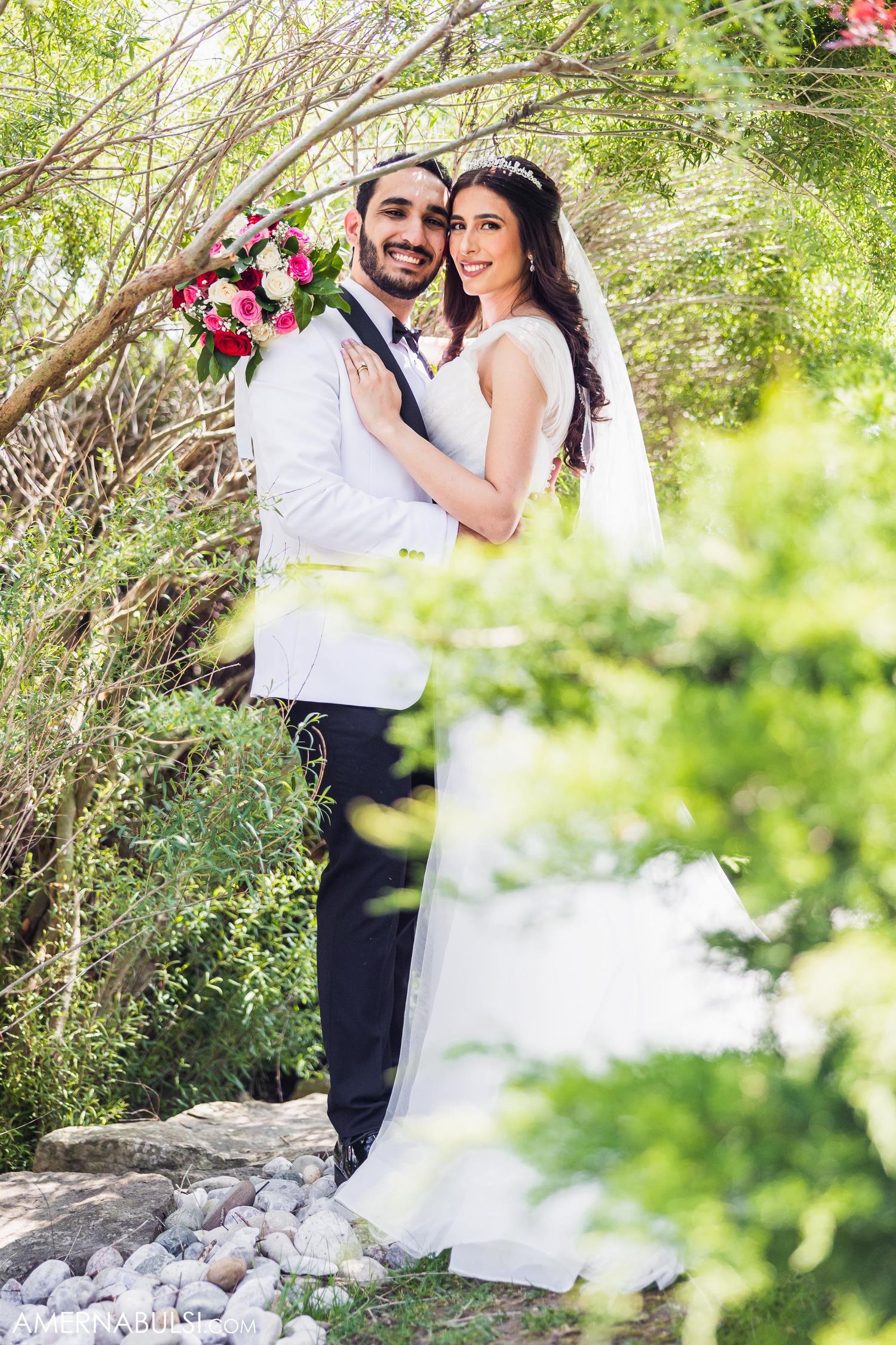 Joyful wedding couple sharing intimate moment among spring blossoms and greenery.