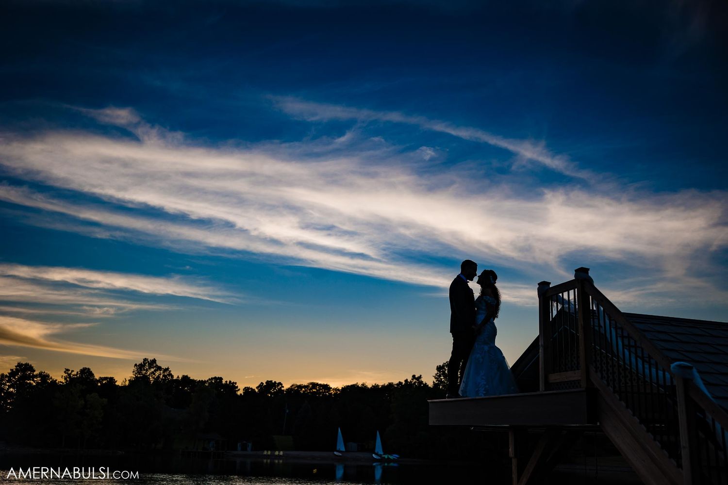 Silhouette of a couple against a dramatic sunset sky on a bridge.