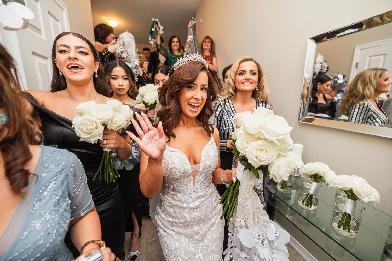 A celebration scene with people holding white bouquets in a mirrored room.