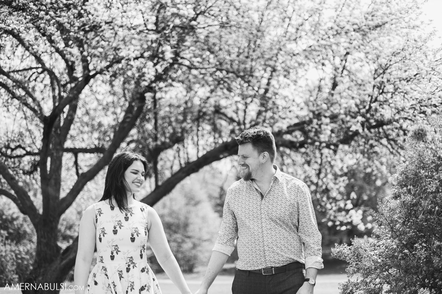 A black and white portrait of a couple sharing a joyful moment under blooming trees.