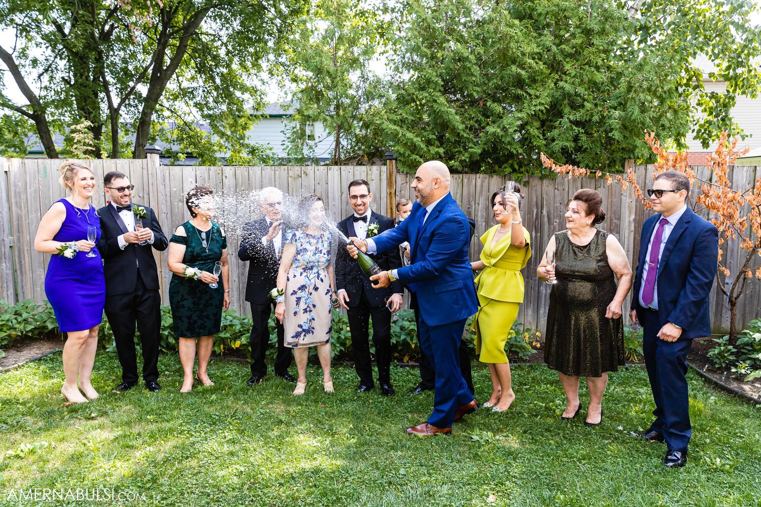 Wedding party in formal attire gathered in backyard garden setting.