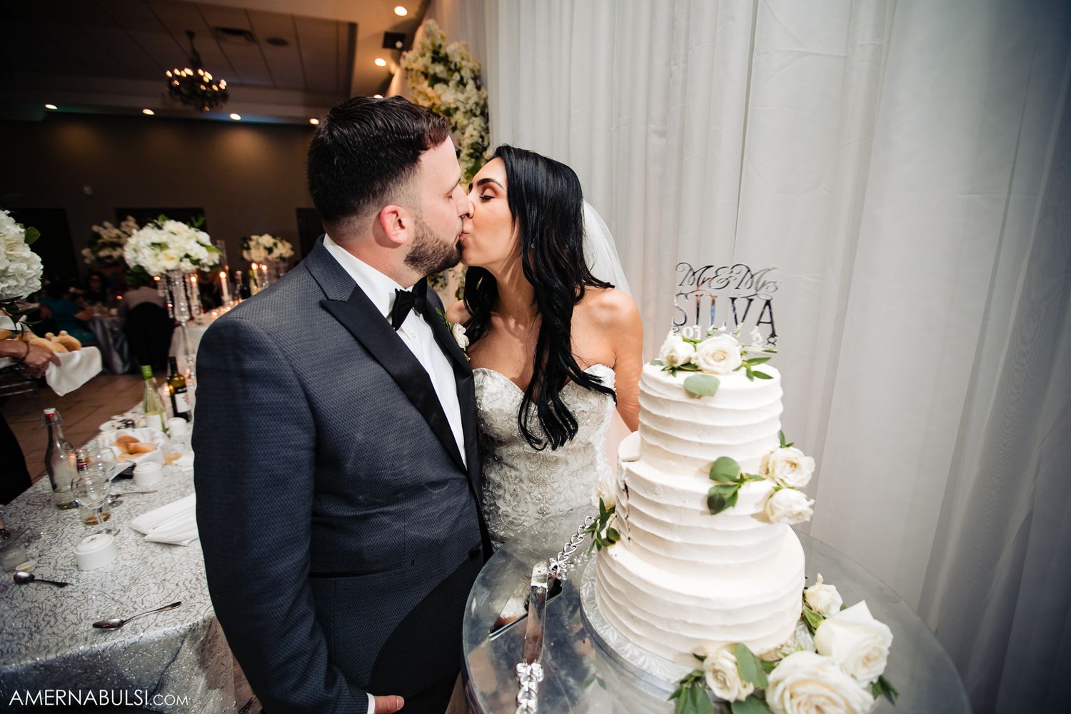 Newlyweds share intimate moments near their wedding cake during an elegant indoor reception.