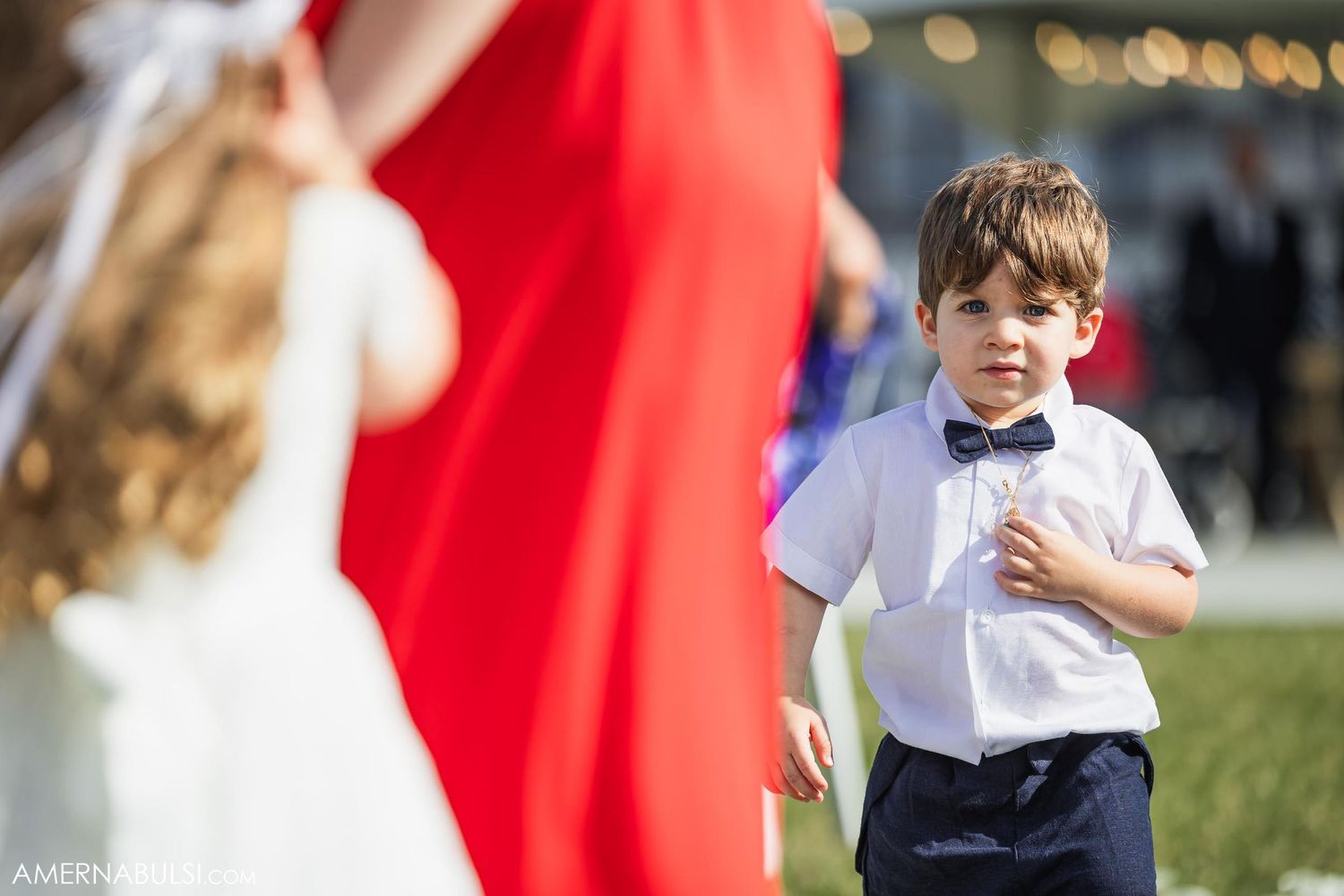 Young attendant in white shirt watching wedding ceremony outdoors.