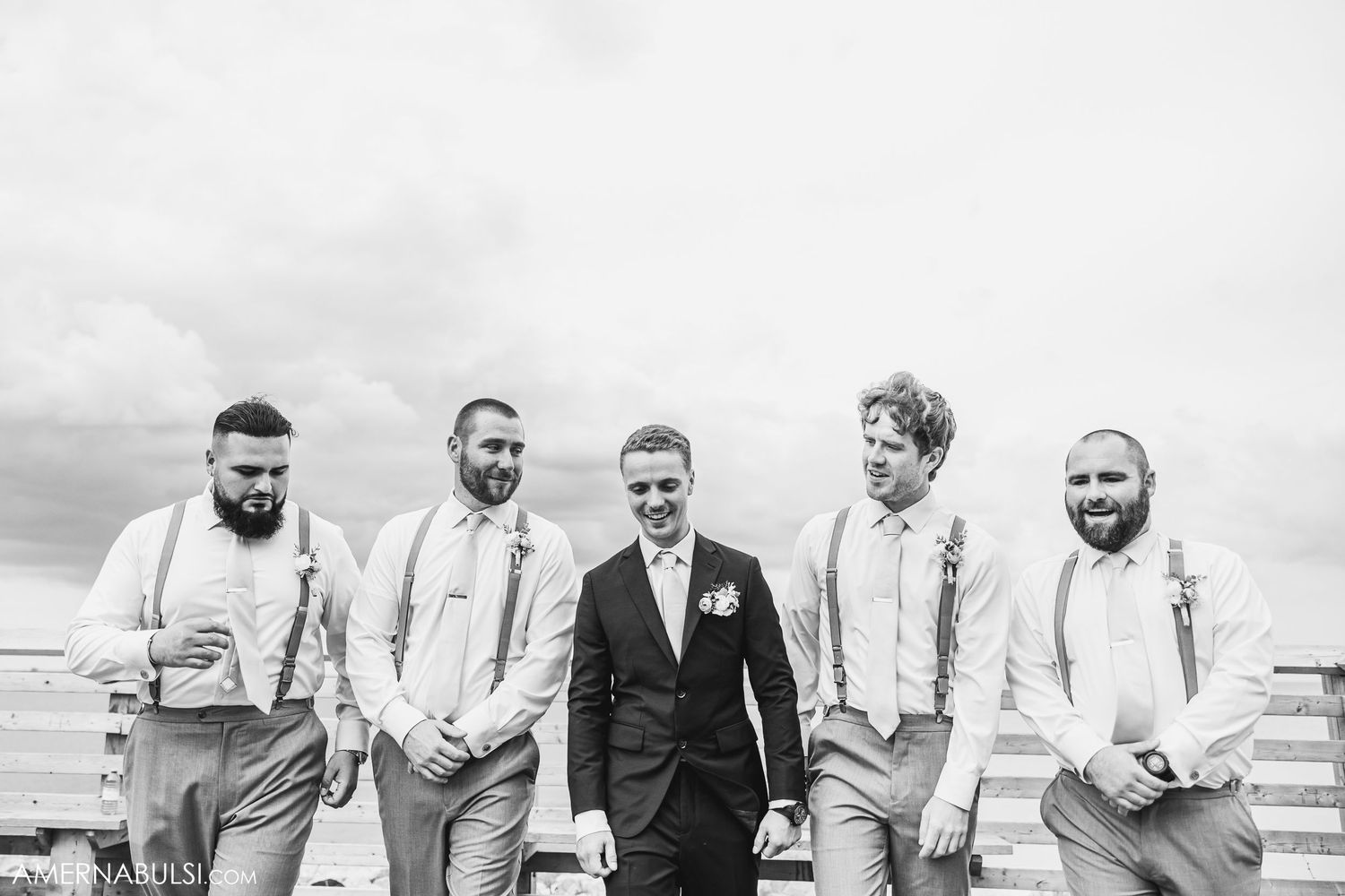 A group of groomsmen in navy suits and light vests laughing together outdoors.