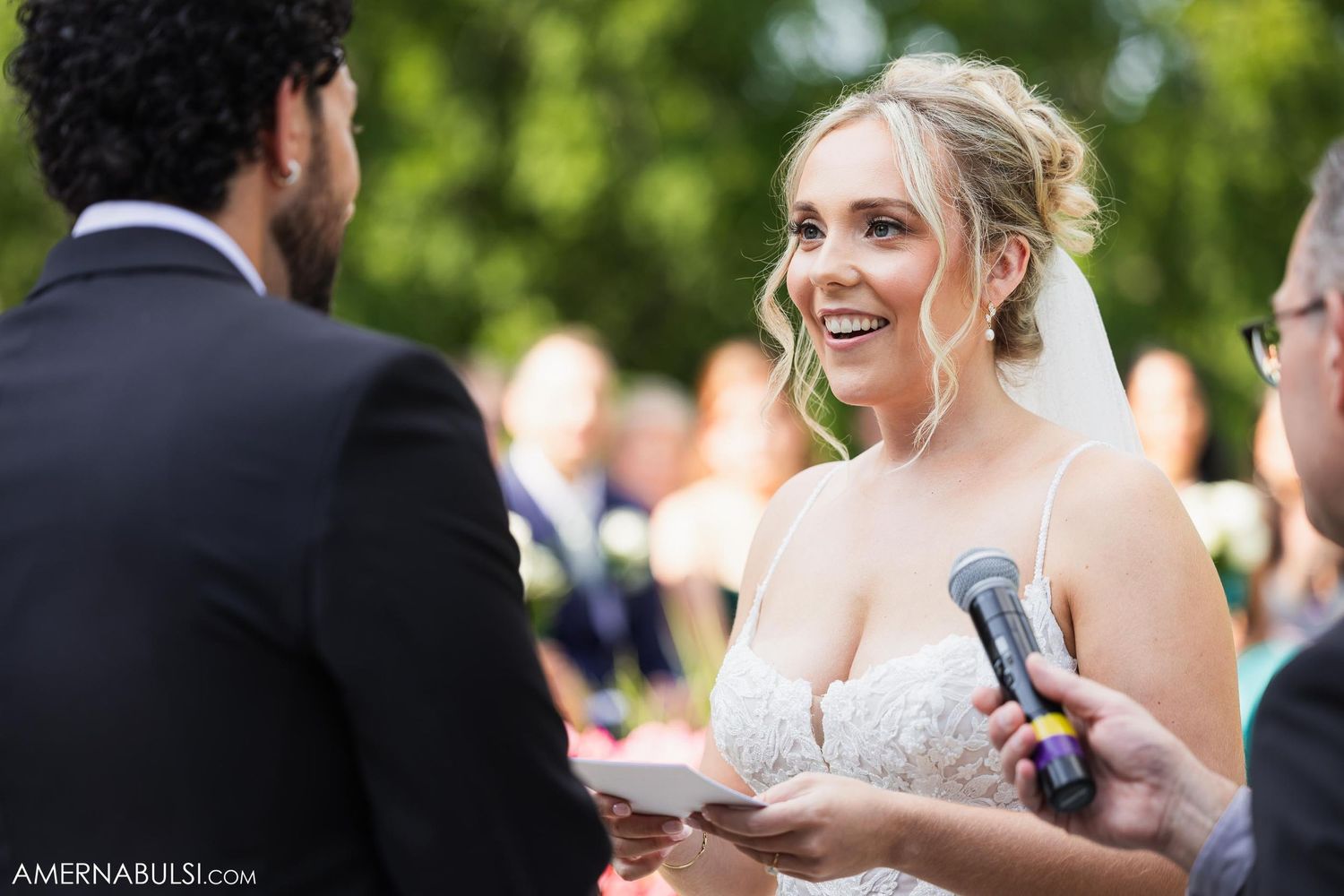 Bride smiling during outdoor wedding ceremony while exchanging vows.