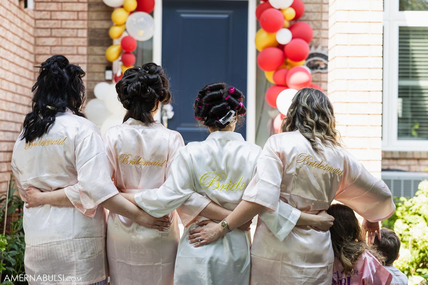 A group in matching white robes stand with their backs to camera and arms around each other.