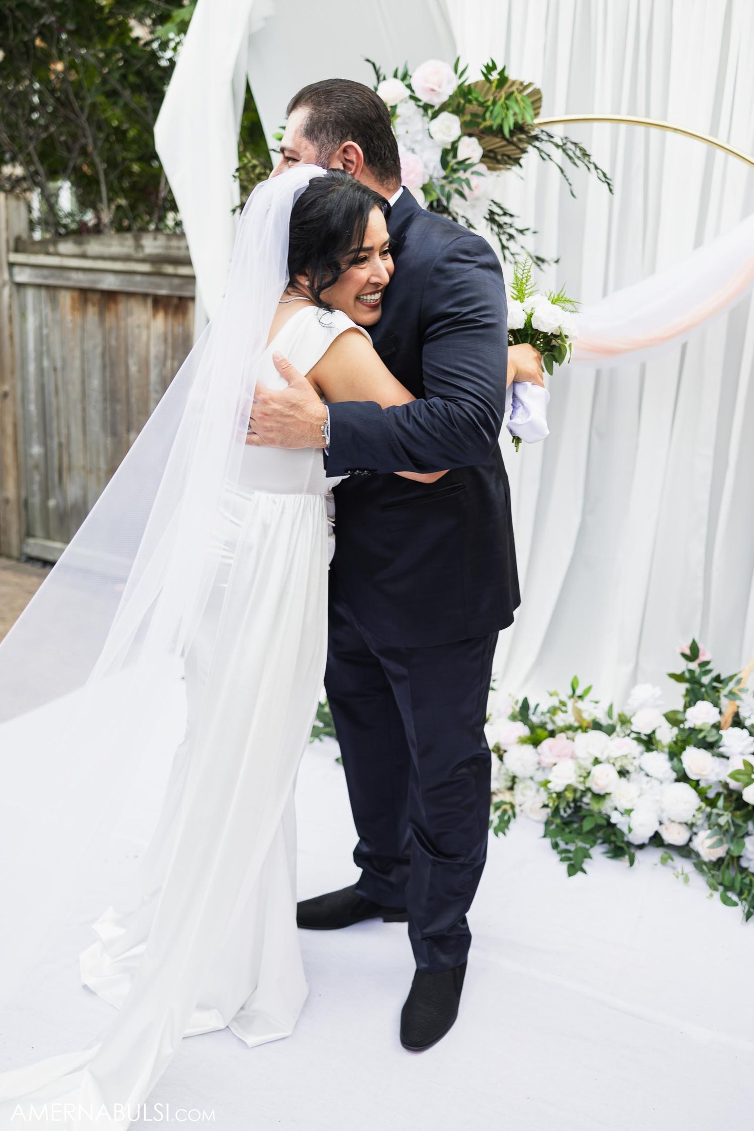 Joyful bride and groom embrace during first look moment at outdoor wedding ceremony.