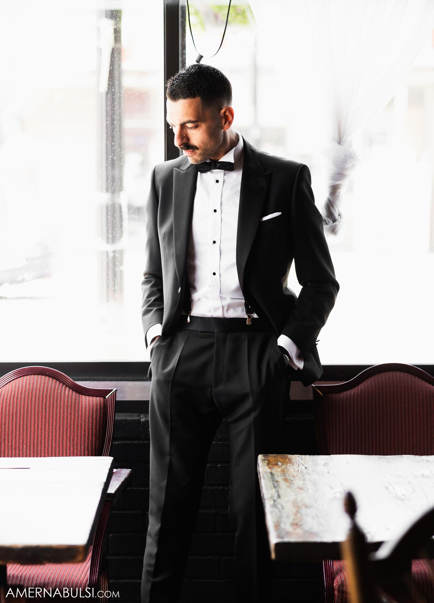 Elegant formal wear portrait in classic black tuxedo by a bright window.