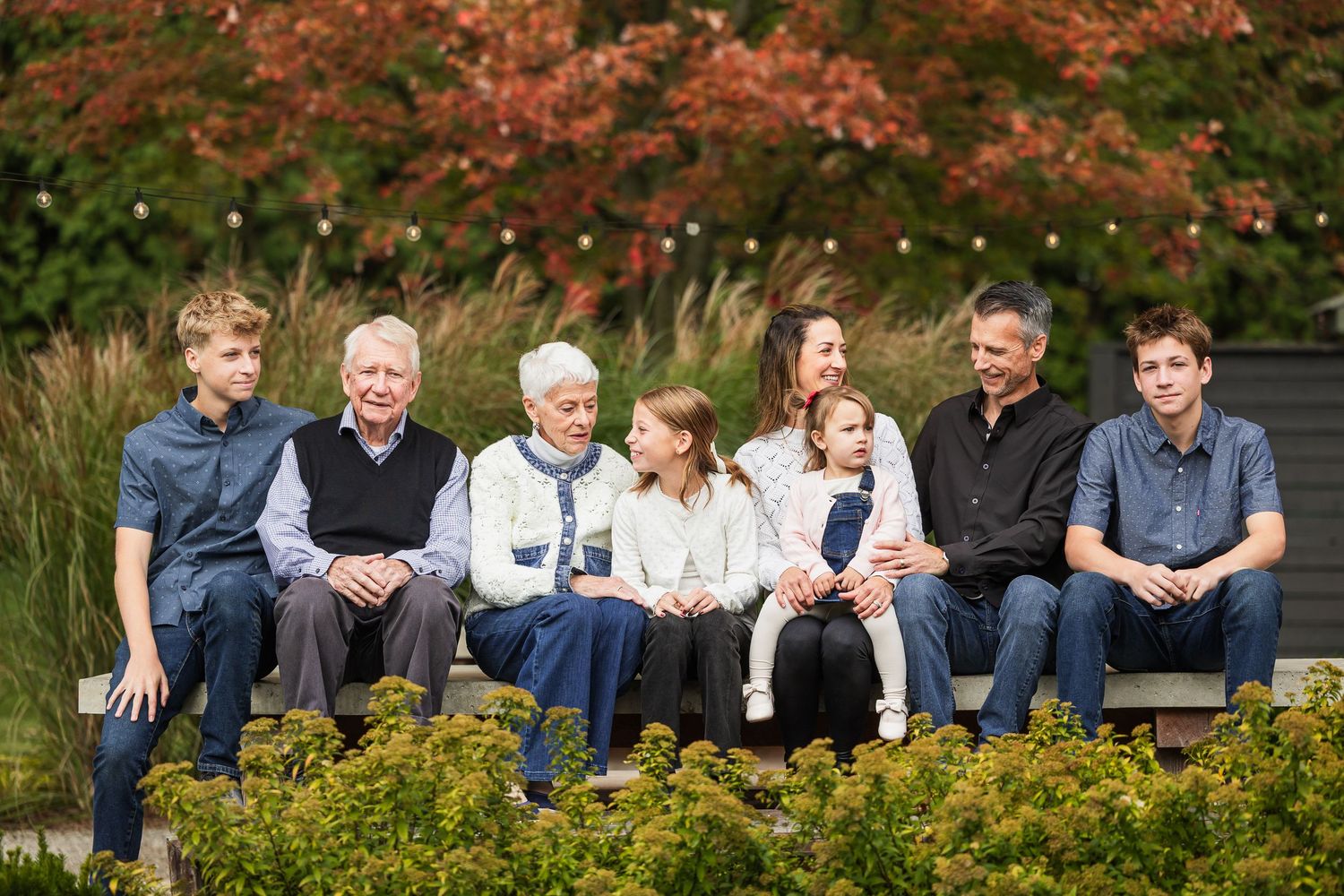 A group of people sitting together on wooden benches in a lush outdoor garden setting.