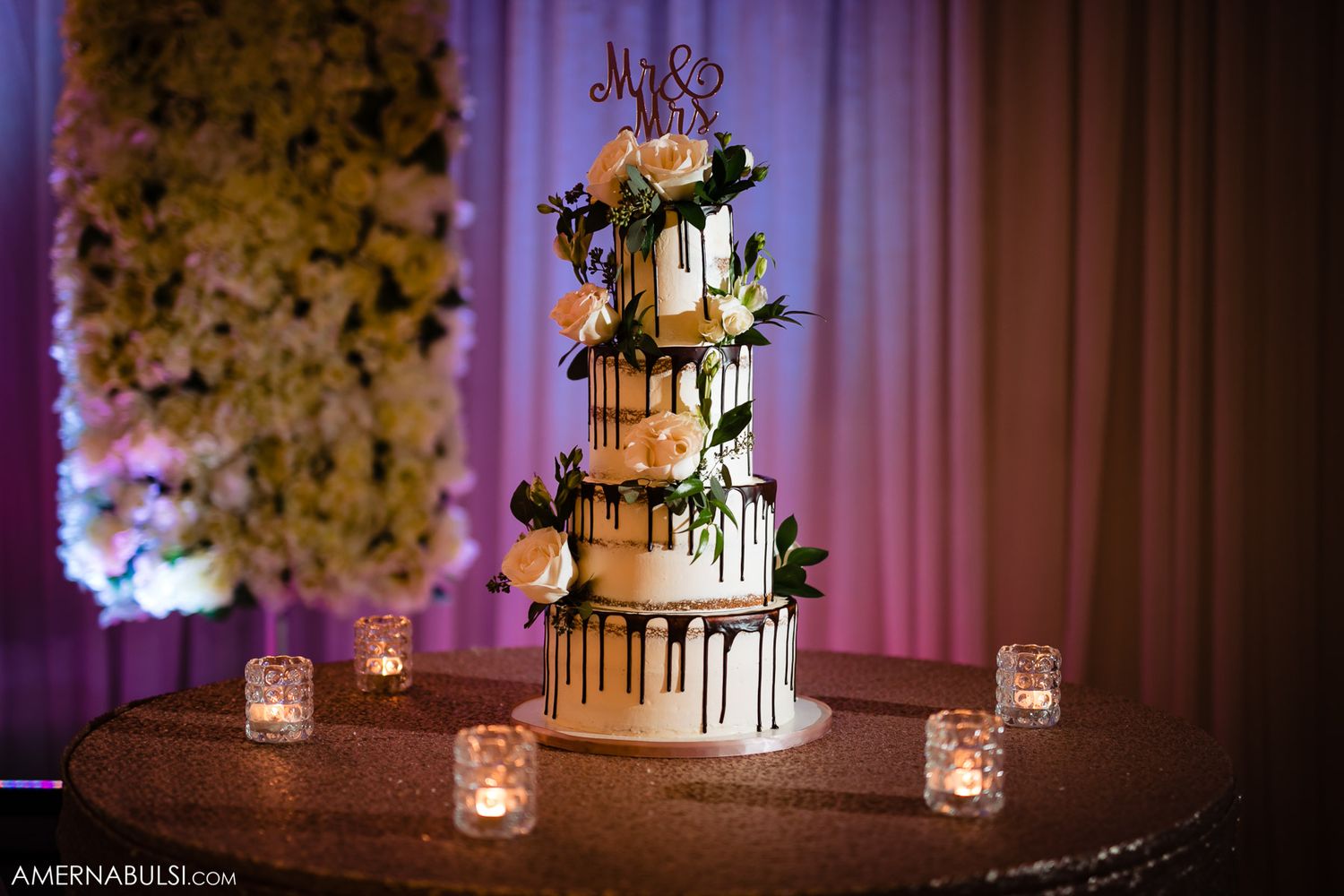 Elegant wedding cake display with dripping details and floral decorations illuminated by romantic candlelight.