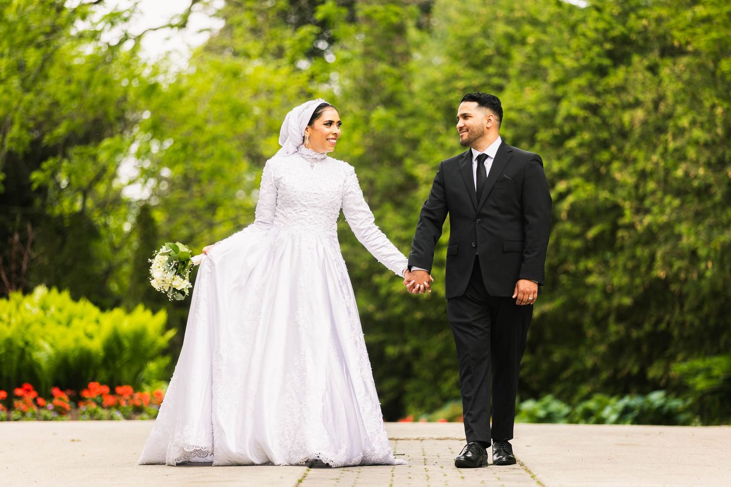 Bride and groom hold hands while walking through garden with colorful flowers.
