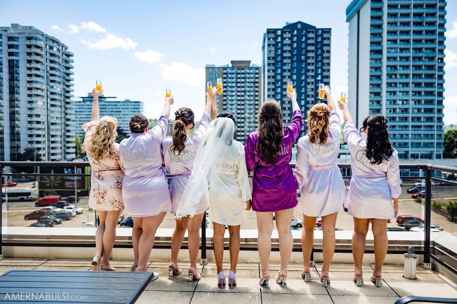 Group wearing matching robes poses with backs to camera overlooking city skyline on rooftop.