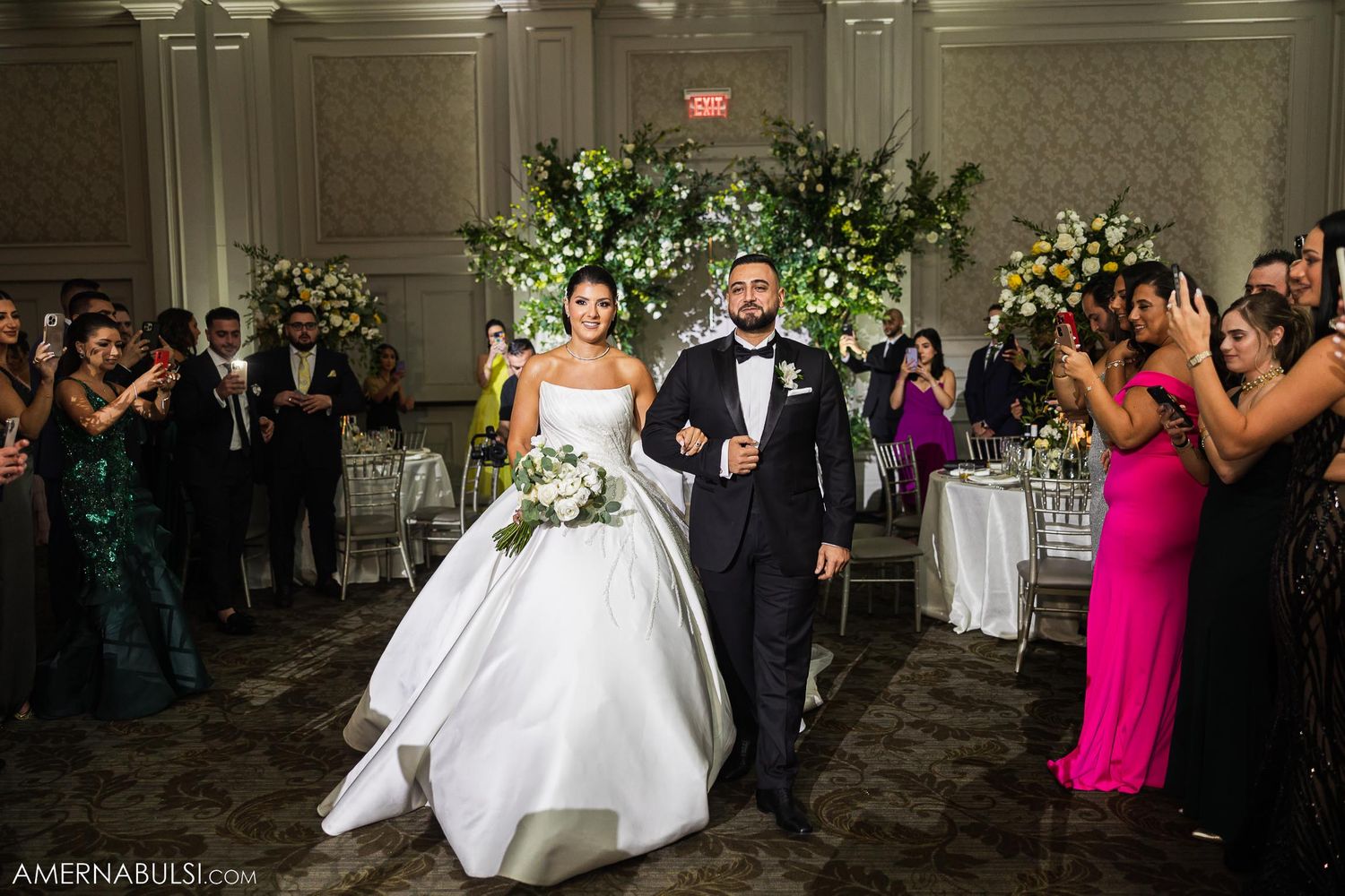 Newlyweds make grand entrance into reception hall as guests applaud.