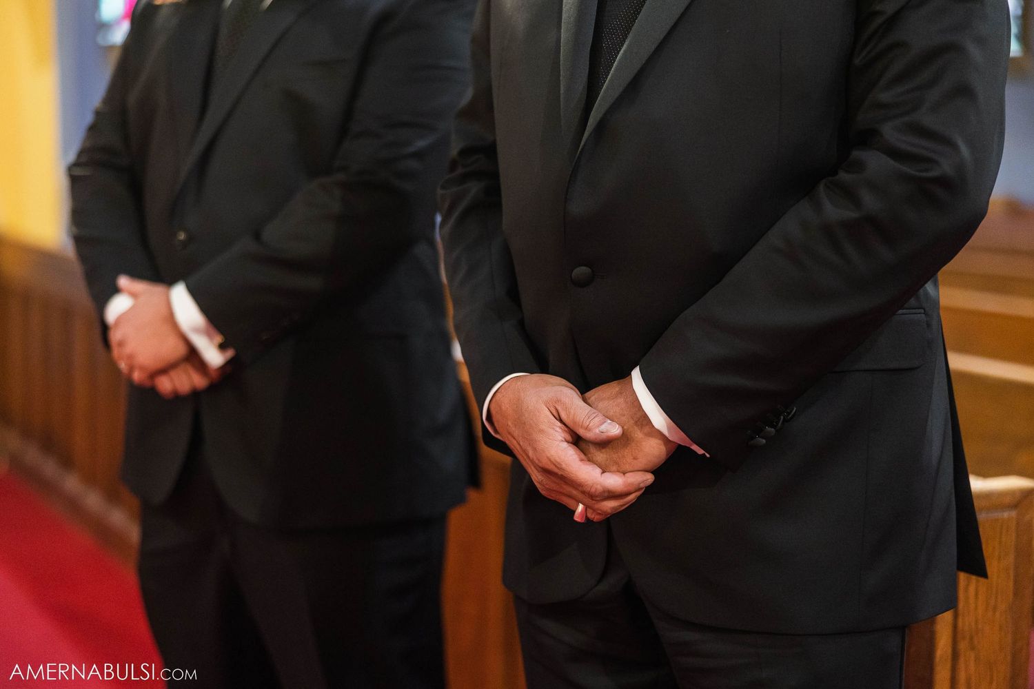 Two men in black suits standing formally in a church.
