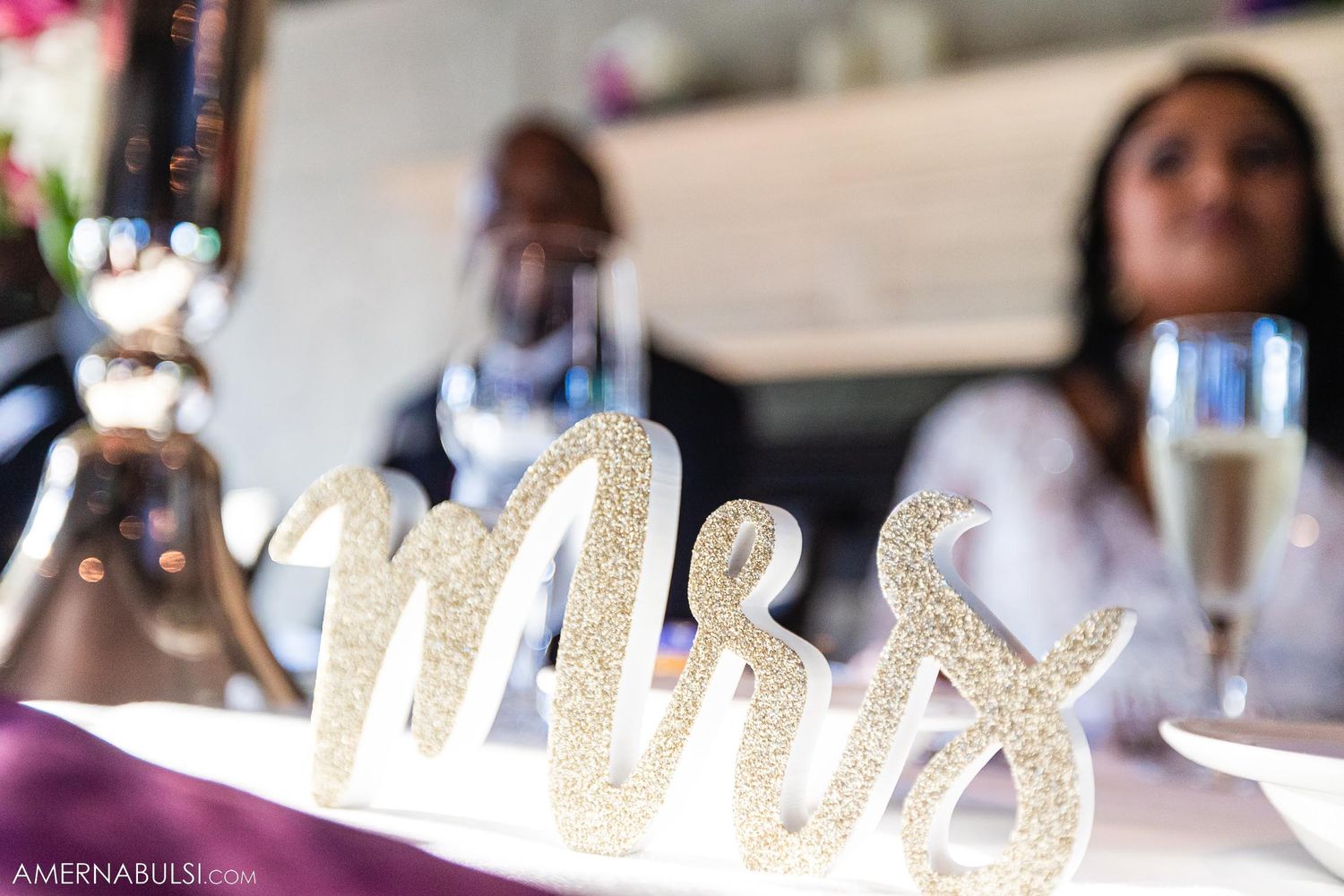 Glittery 'Mr & Mrs' wedding sign decoration on a table with champagne glasses.