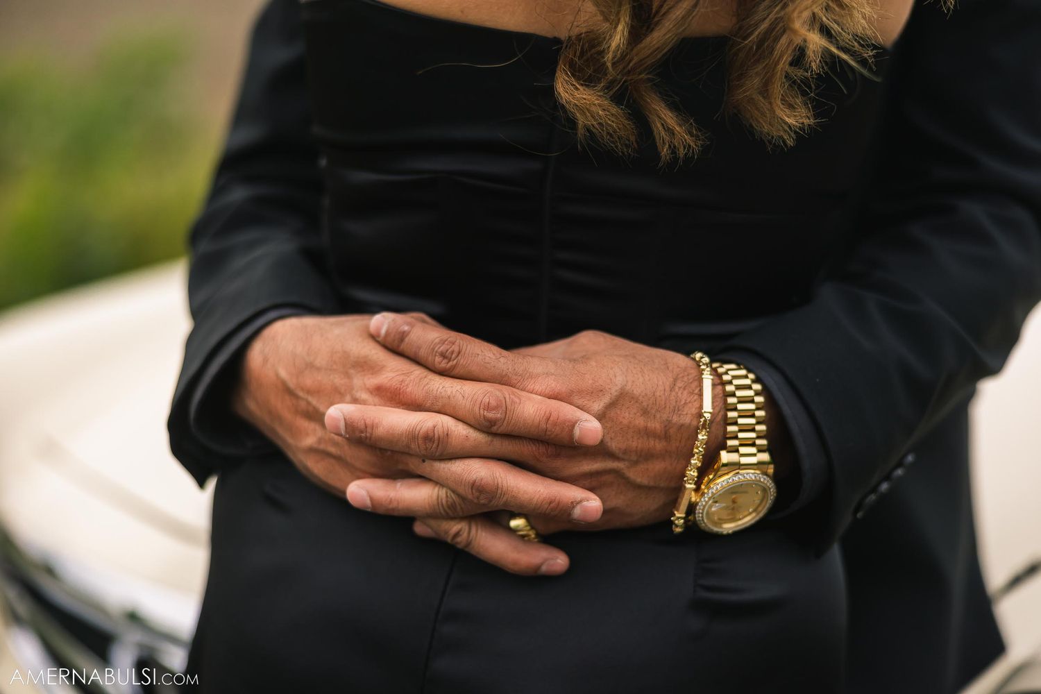 Close-up of hands with gold watch embracing against formal attire.