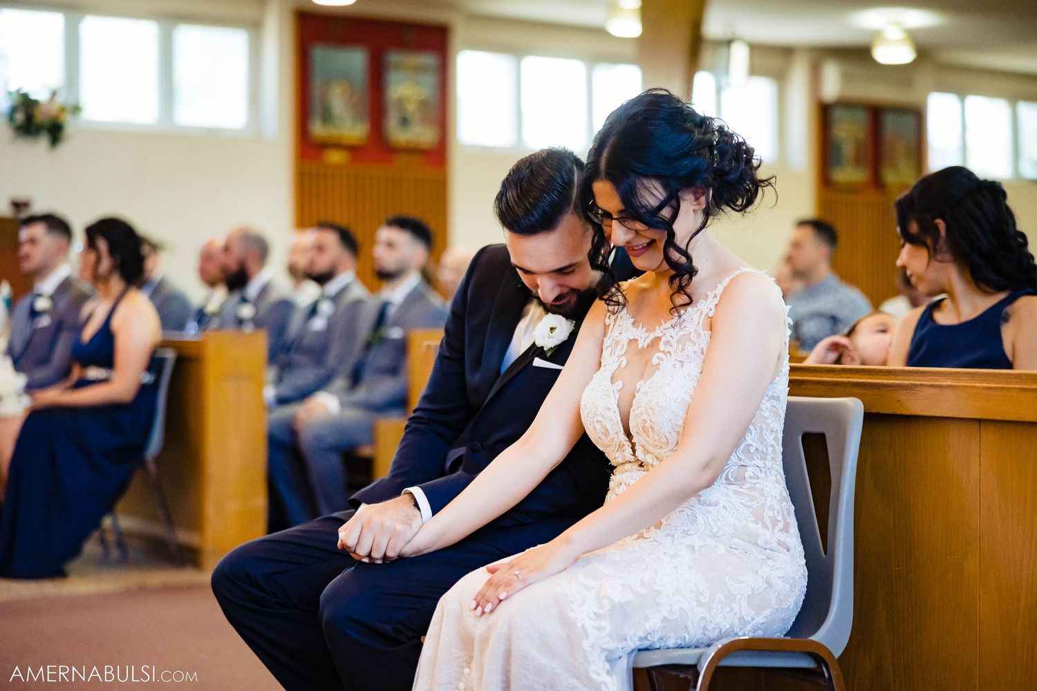 Couple sitting close together in wooden church pews during wedding ceremony.