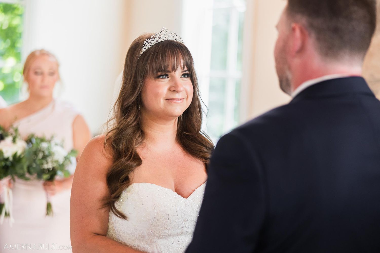 Bride in a white strapless gown and tiara gazes lovingly during the wedding ceremony.