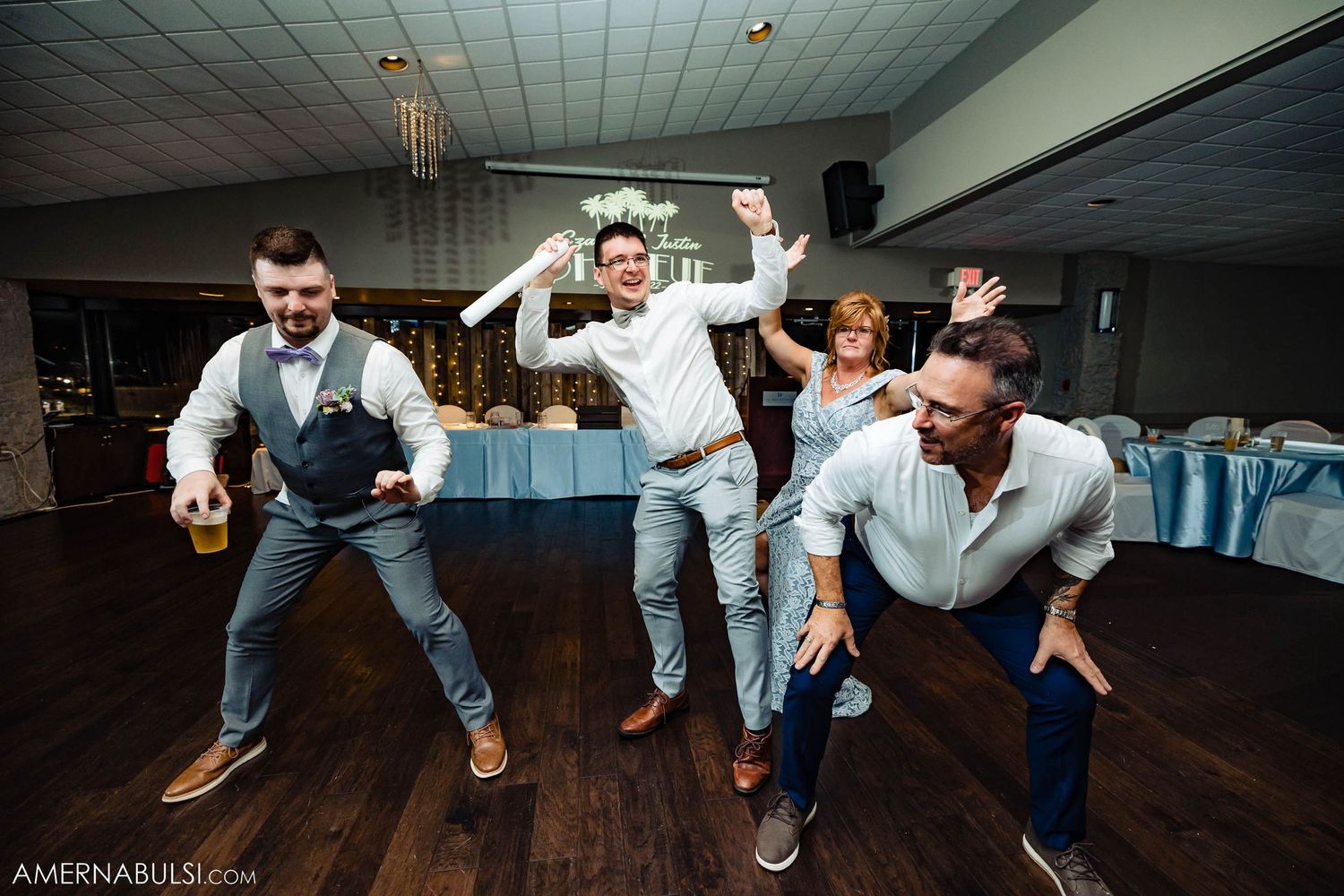 Energetic groomsmen showing off dance moves at a wedding reception on hardwood floor.