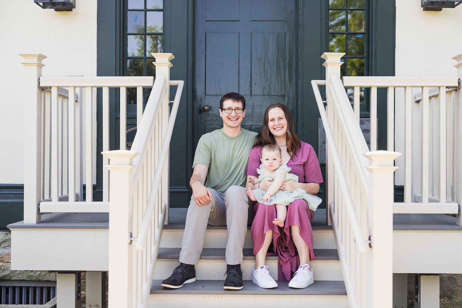 Family sitting together on white porch steps of house with blue door.