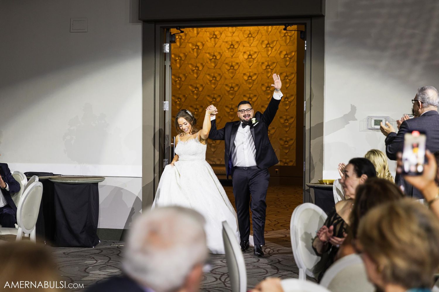 Grand entrance celebration with raised arms and cheering guests at wedding reception venue.