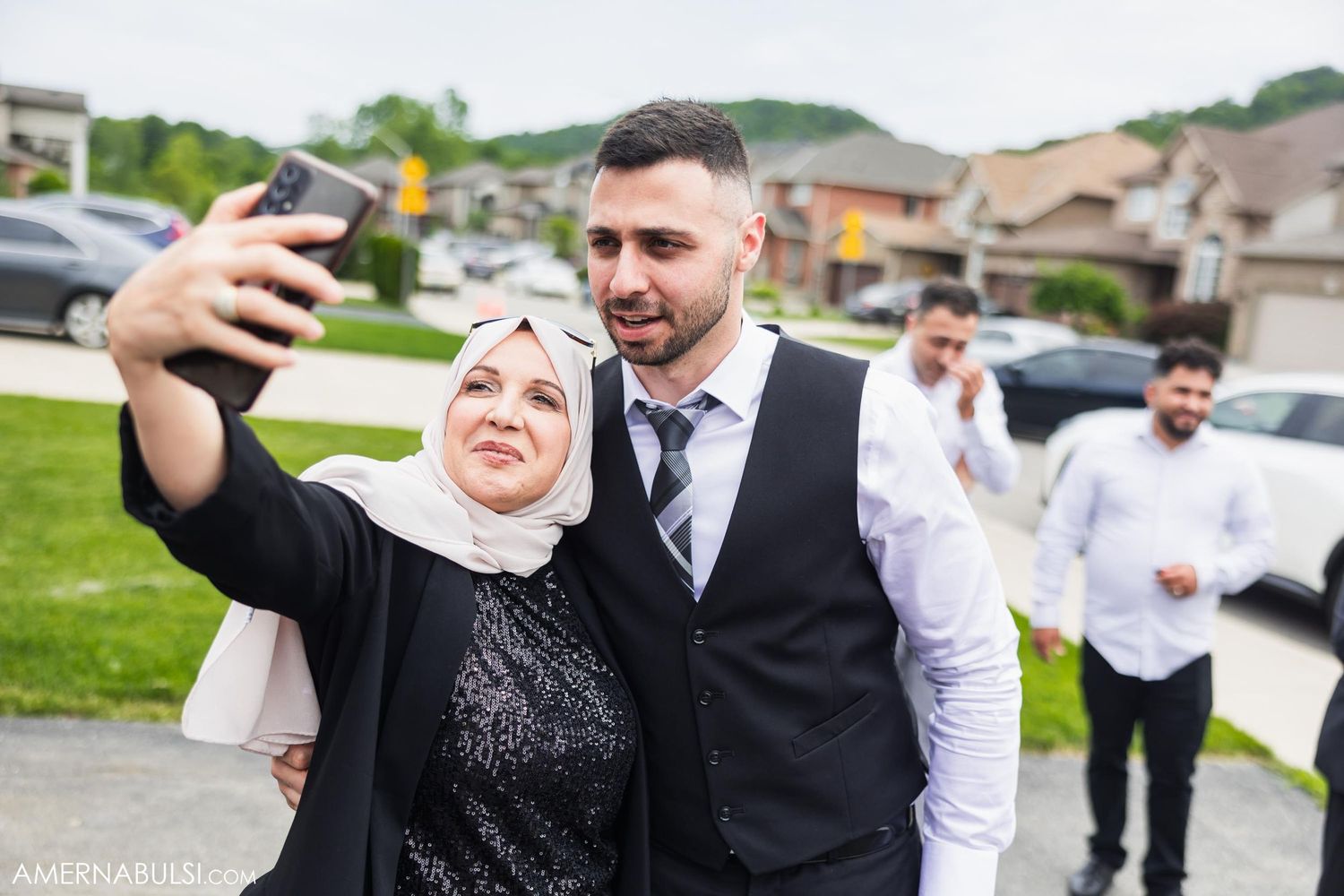 Wedding guest and groomsman take a celebratory selfie during outdoor reception.