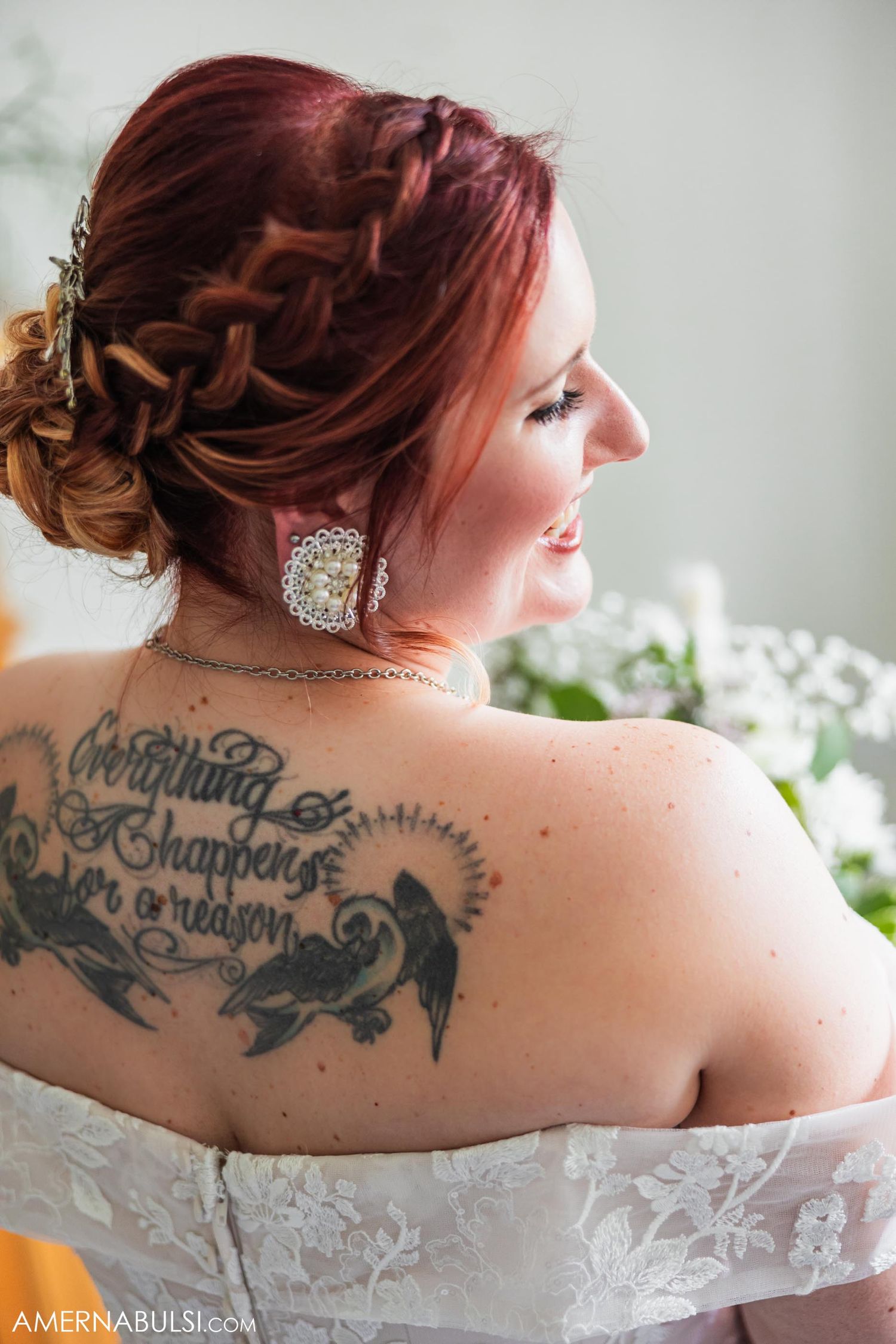 Intricate braided updo and detailed back tattoo visible above a white lace wedding dress.