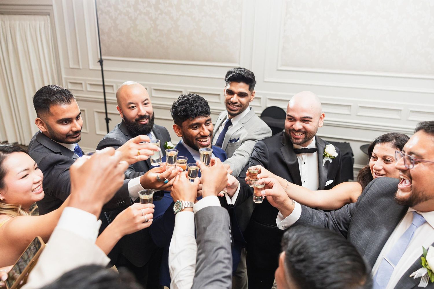 Wedding party members raise glasses in celebratory toast circle.