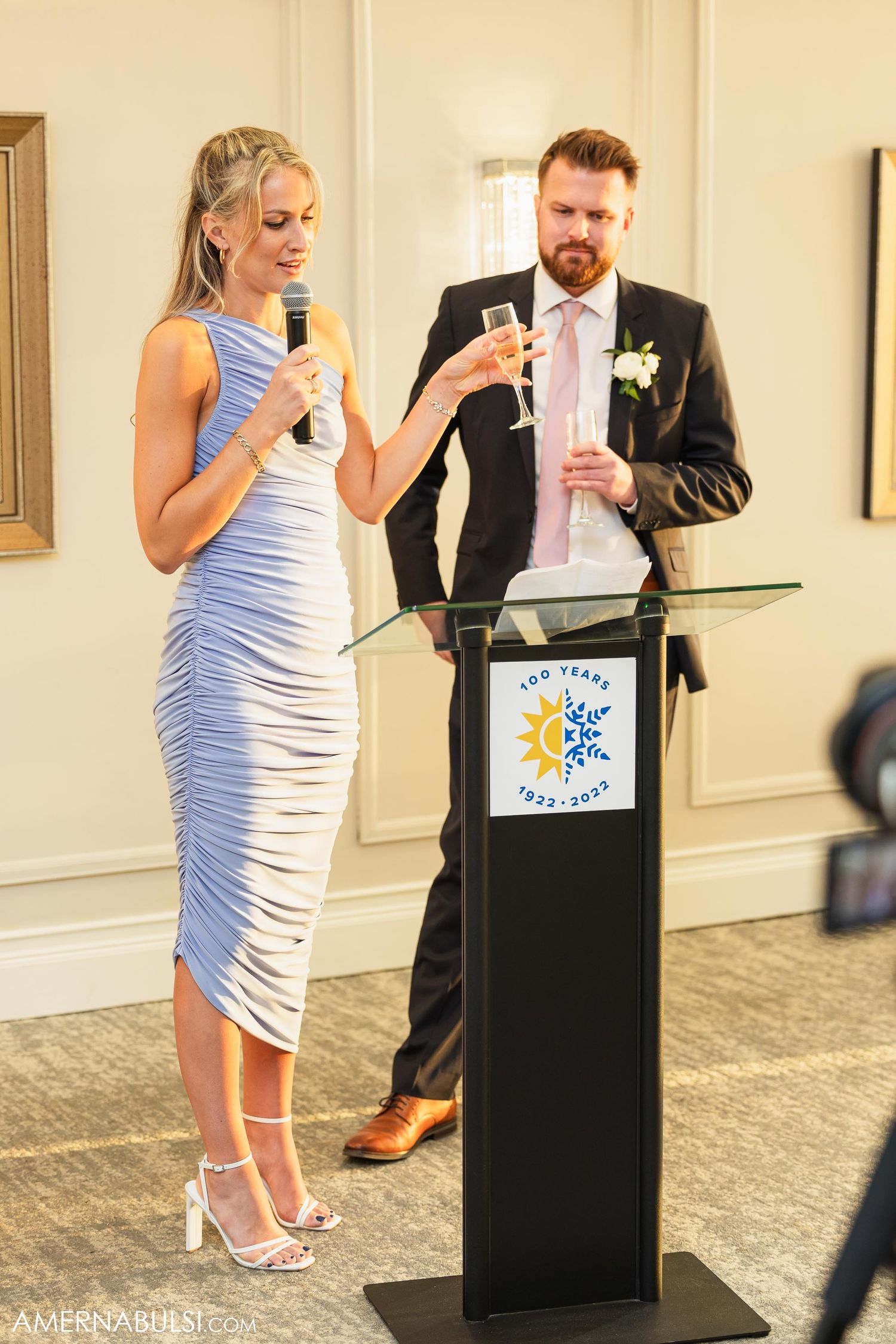 Wedding speakers deliver toasts at a podium with champagne glasses in hand.