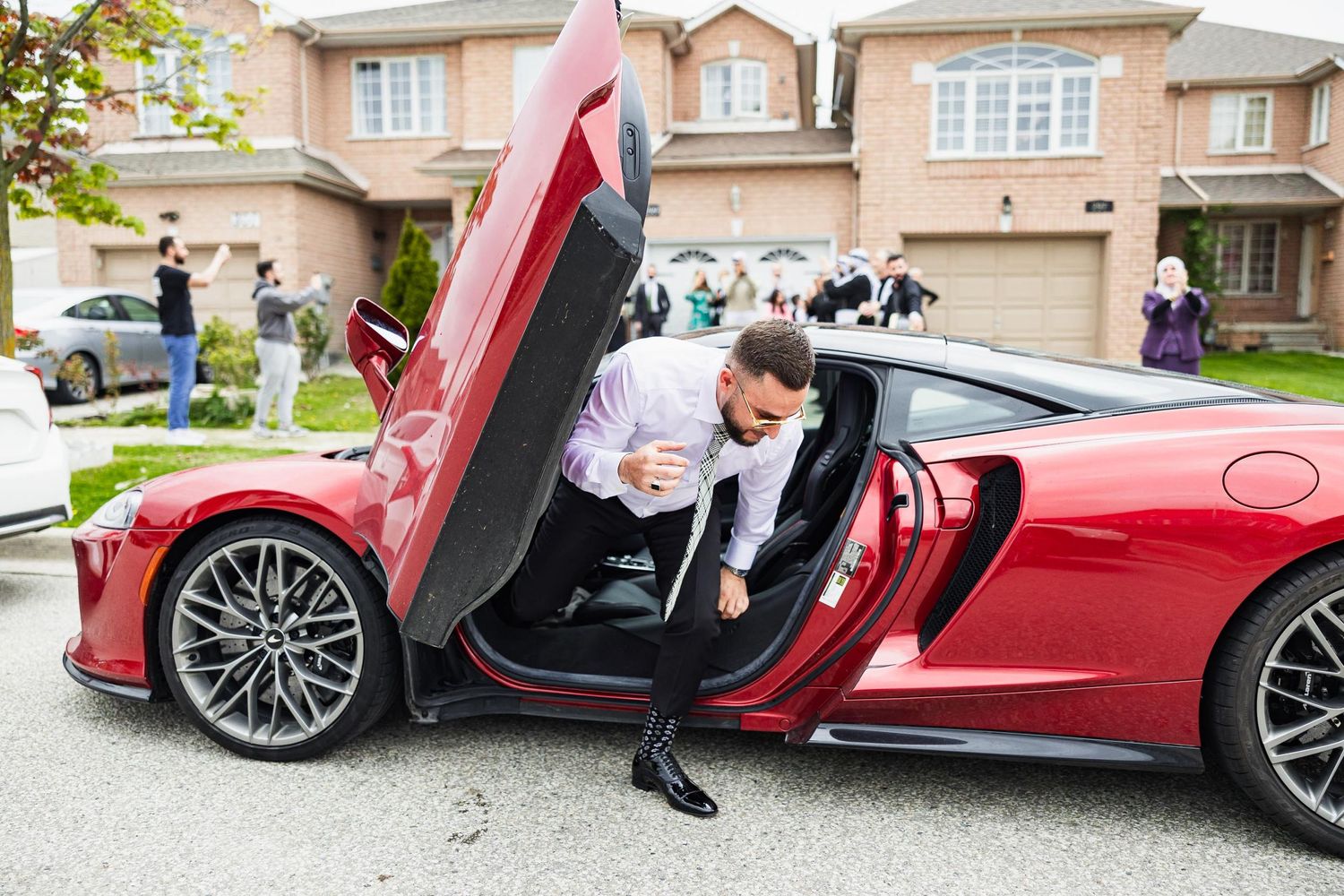 Person stepping out of red luxury sports car with scissor doors in residential driveway.