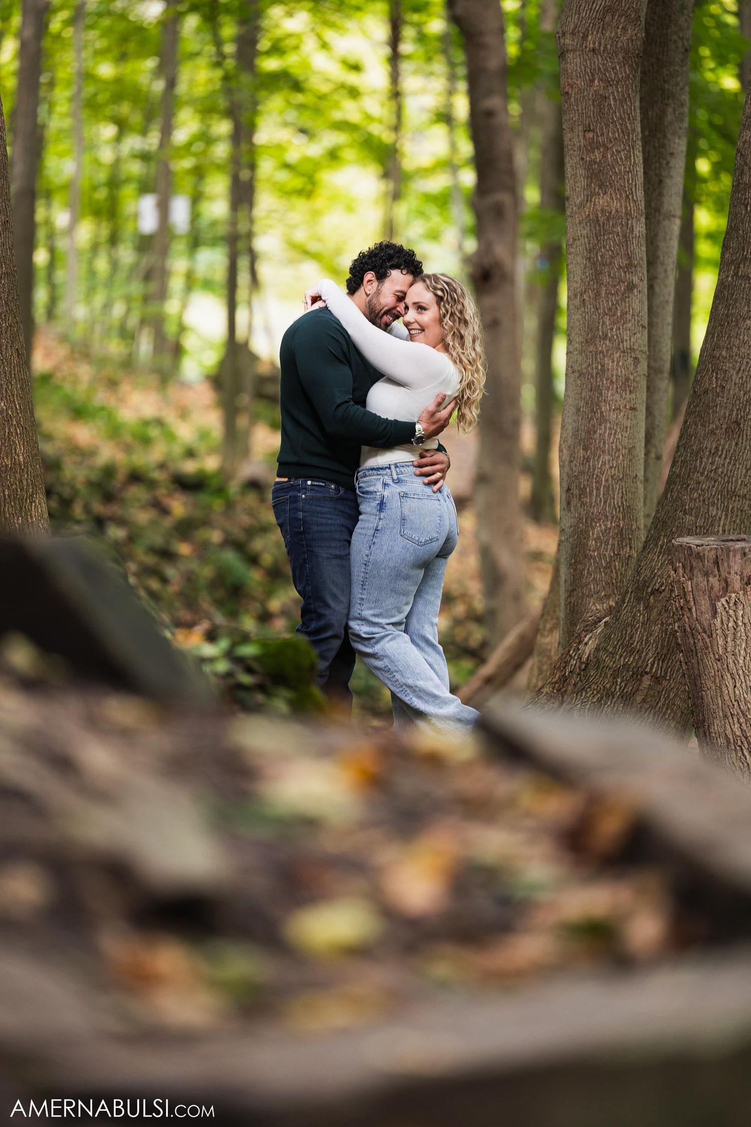 A tender embrace between a couple standing among tall trees in an autumn forest.