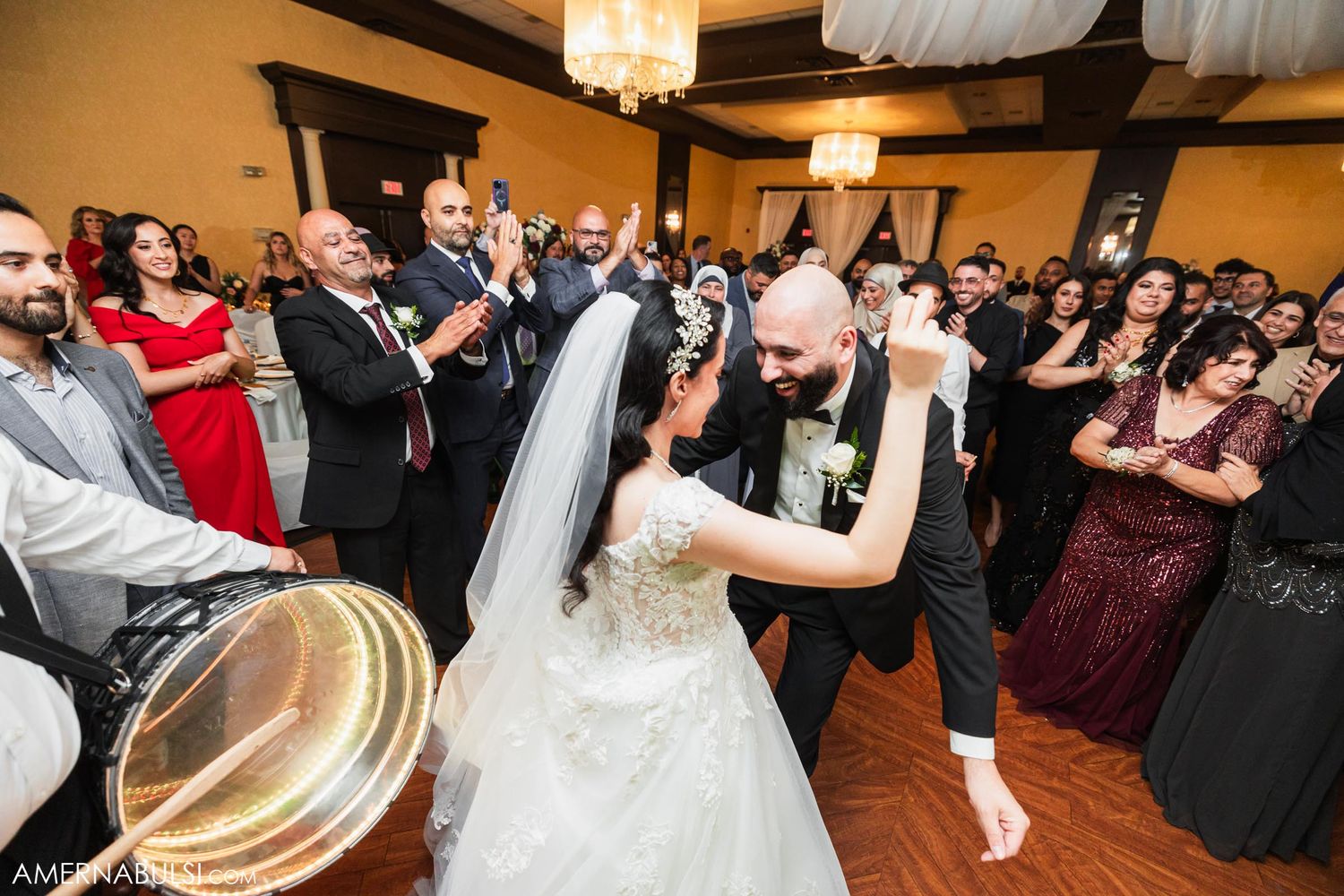 A couple shares their first dance while guests clap and musicians play percussion instruments.