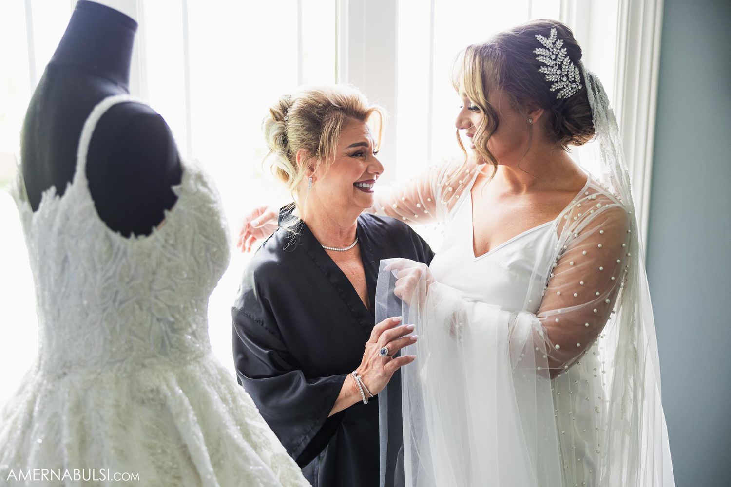 A wedding dress on display stands beside two people sharing a joyful moment.
