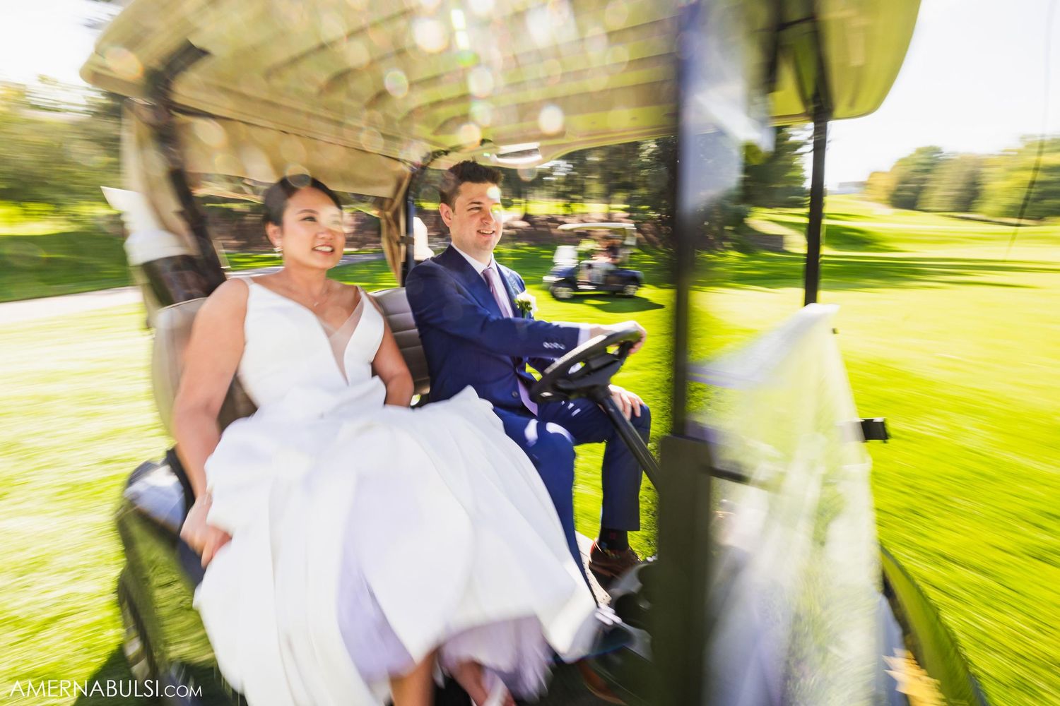 A couple riding in a golf cart through a sunny course on their wedding day.