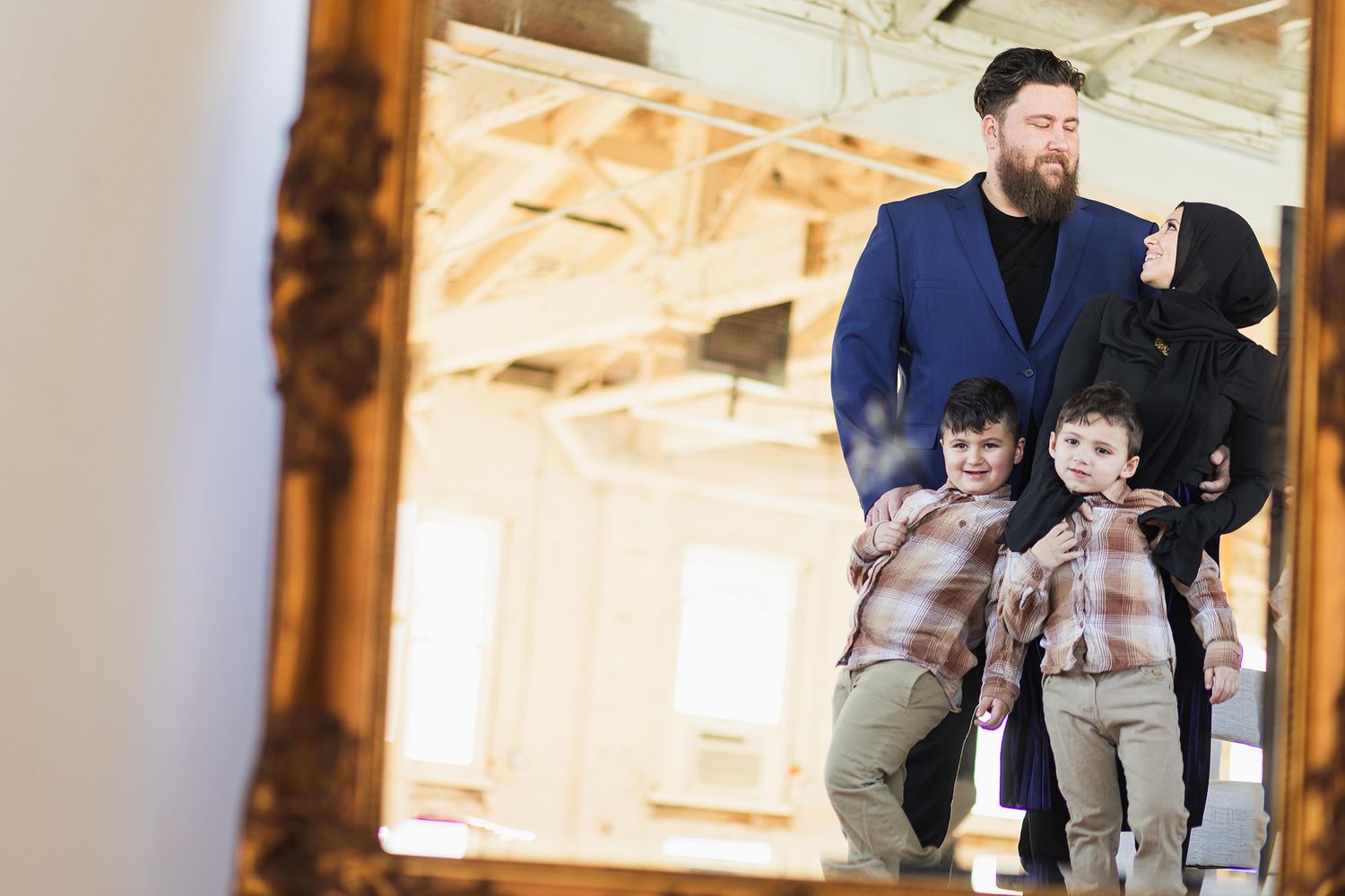 A mirror reflection shows a family group in casual attire standing together in an indoor setting.