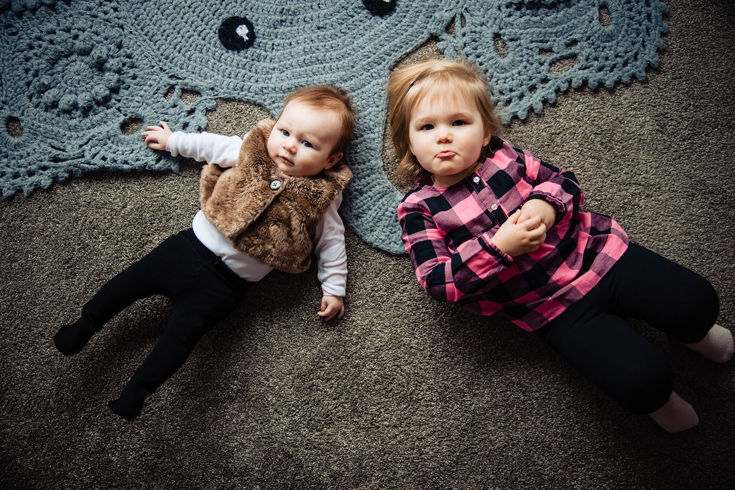 Two small children lying on a carpet next to vinyl records making silly expressions.