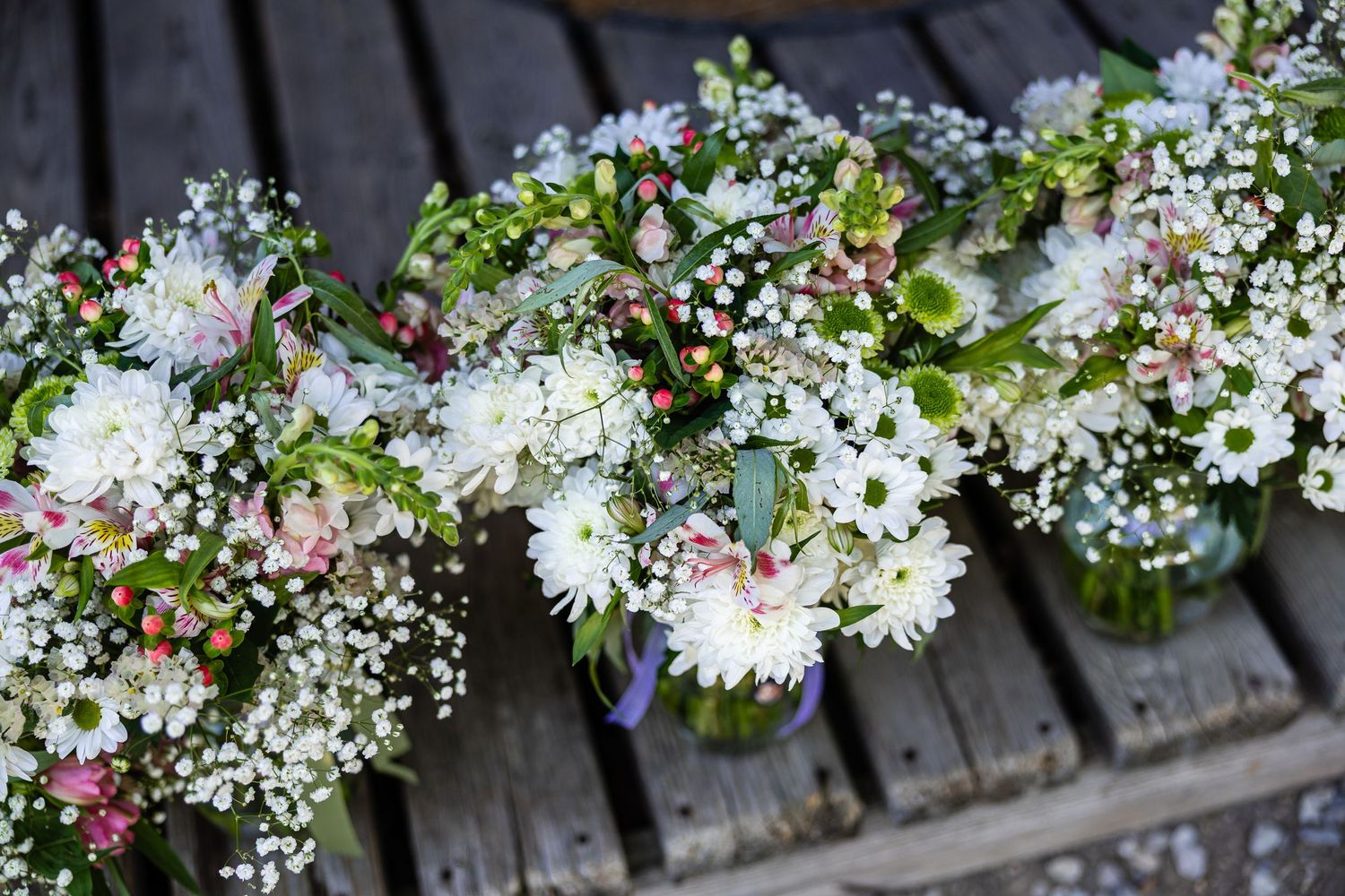 Fresh white and pink wildflower bouquets with baby's breath arranged on a rustic wooden table for a wedding.