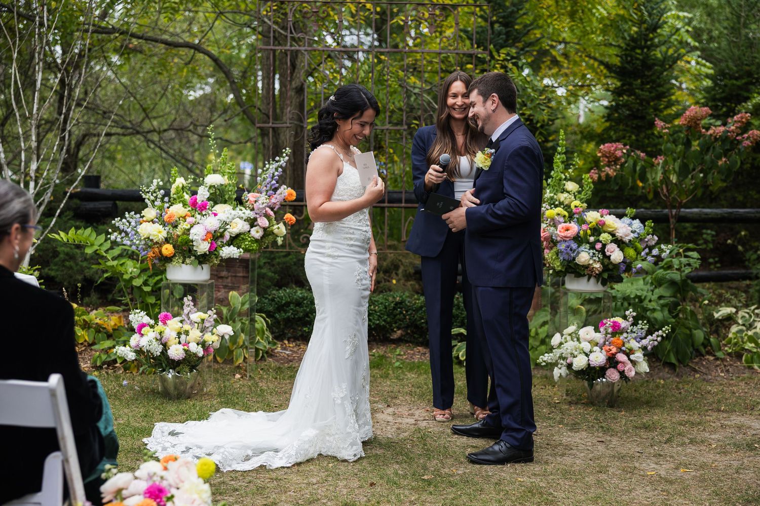 Bride and groom exchange vows at outdoor wedding ceremony with vibrant floral arrangements in background.