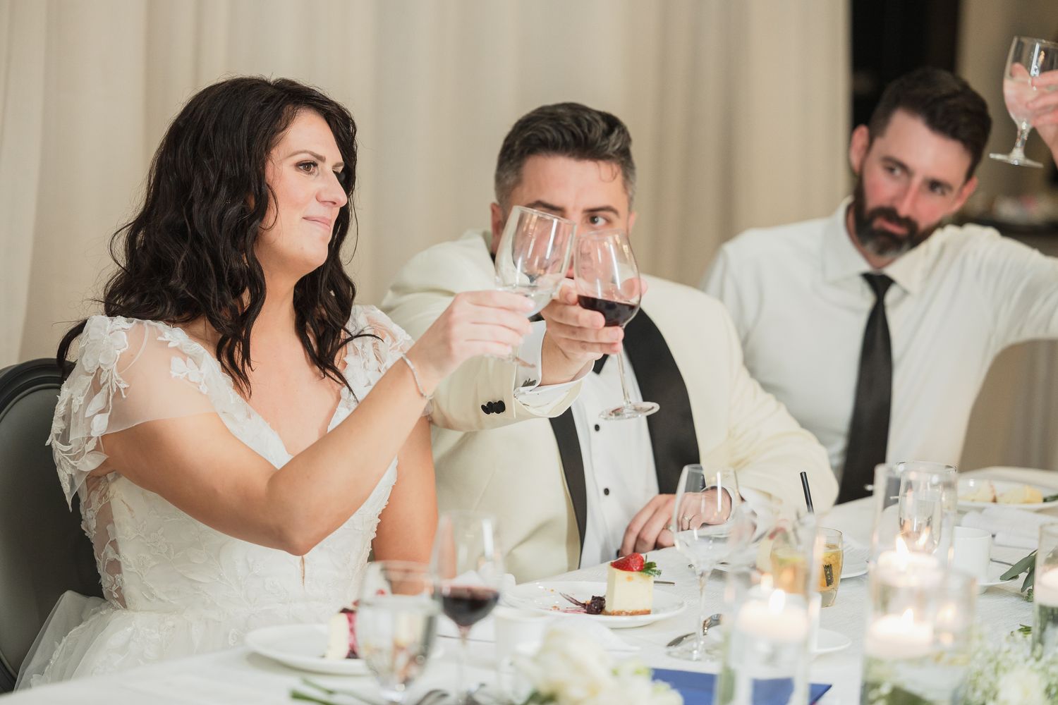 Bride and groom raising wine glasses in a toast at their elegant wedding reception dinner.