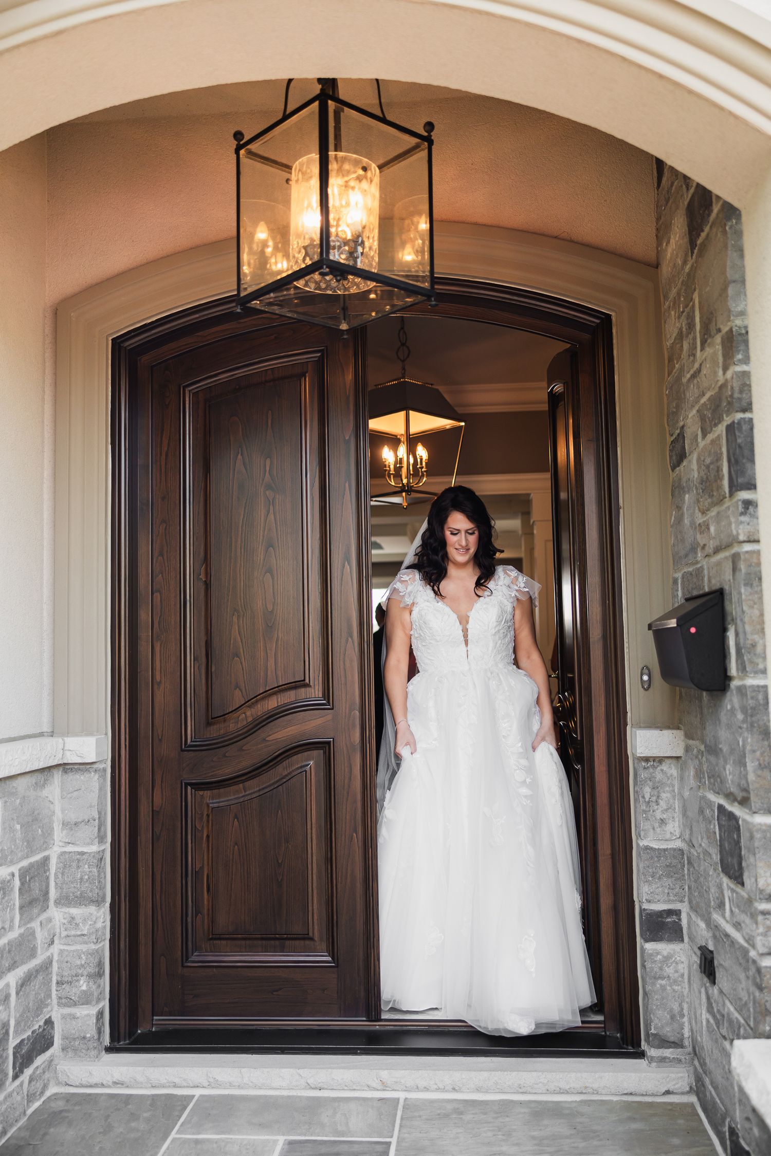 Bride in a white lace ball gown standing in an elegant arched doorway with lantern lighting.